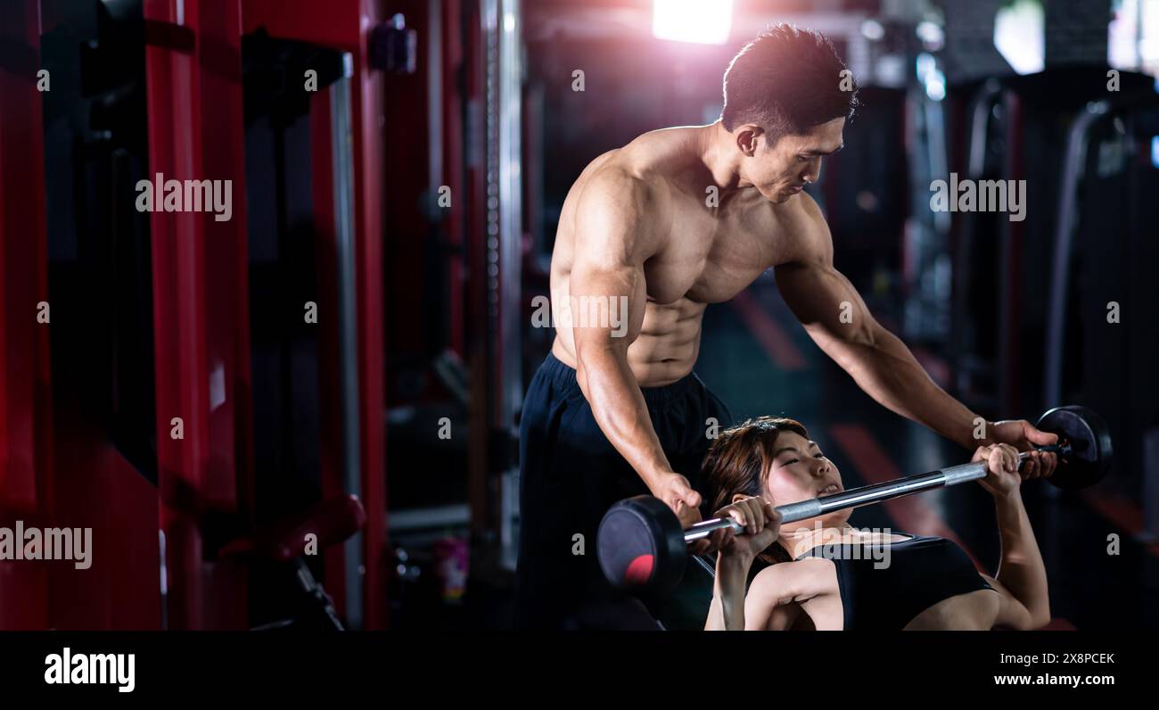 L'allenatore asiatico sta introducendo l'uso di un barbell a uno studente in palestra, allenandosi con il sollevamento di potenza Foto Stock