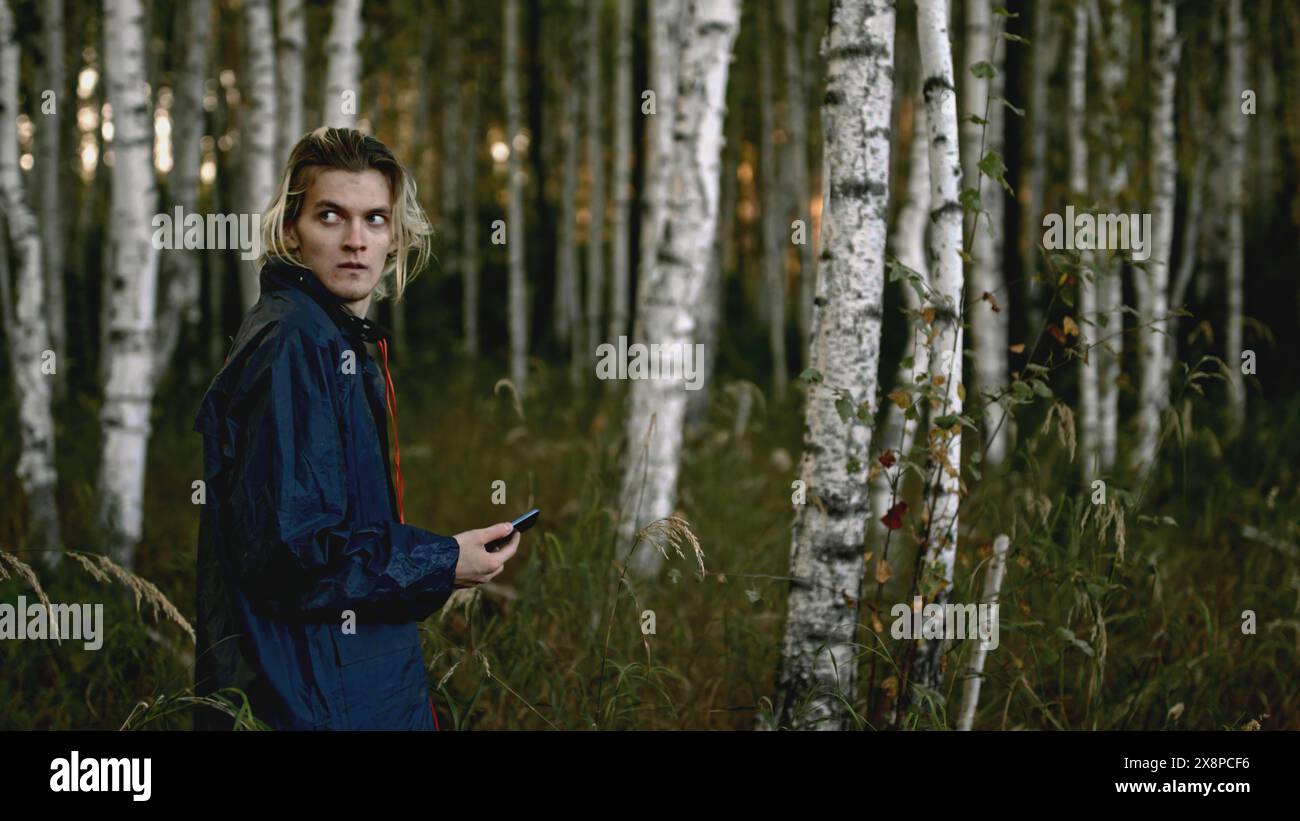 L'uomo vaga nella foresta e si guarda intorno ansiosamente. Stock. Il giovane cammina nel bosco con il telefono e si guarda intorno ansiosamente. L'uomo si è perso nel bosco con Foto Stock