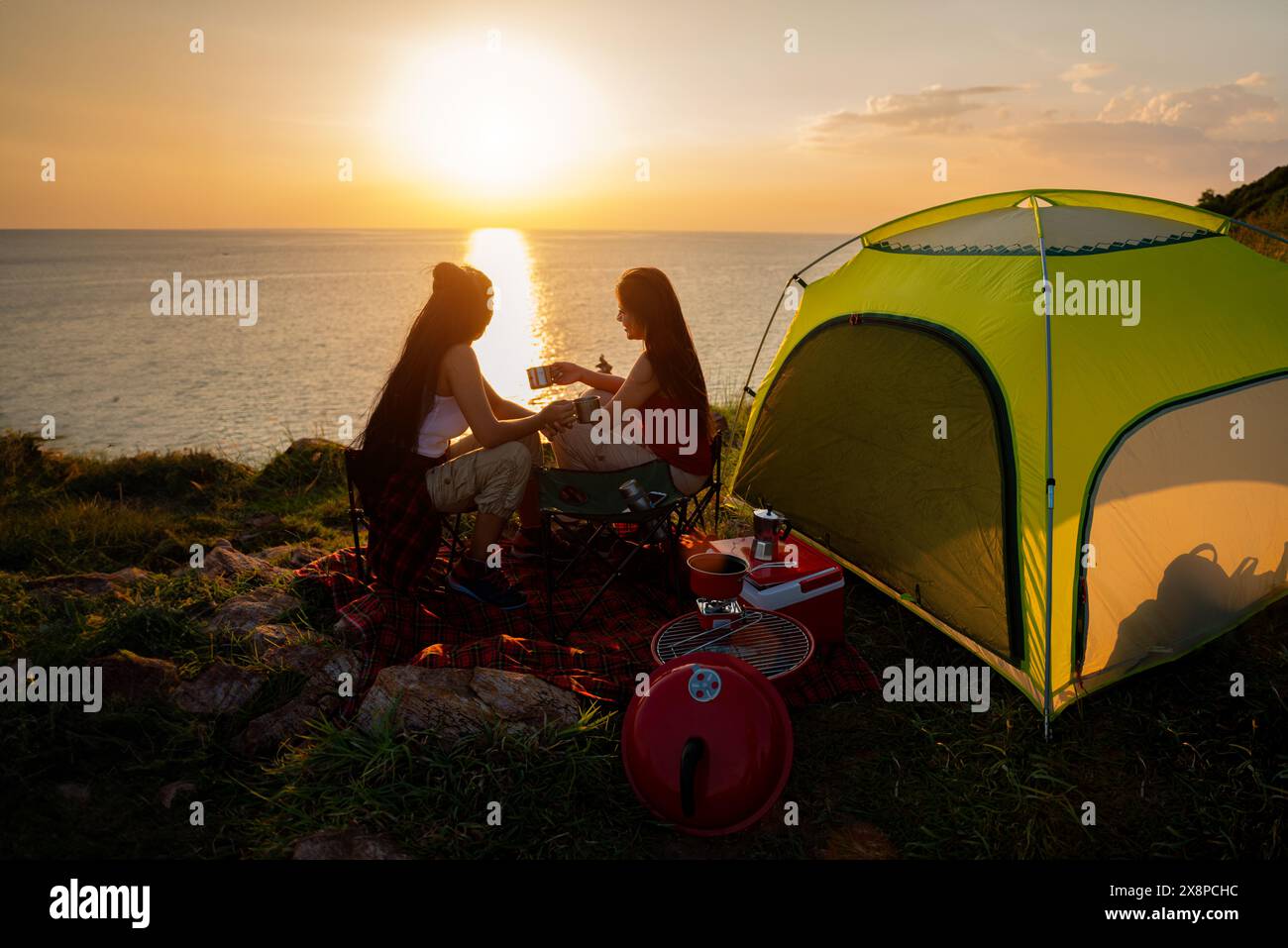 Due escursioniste si accamparono su una scogliera sul mare. Le escursioniste bevono un caffè mentre si godono il tramonto. Foto Stock