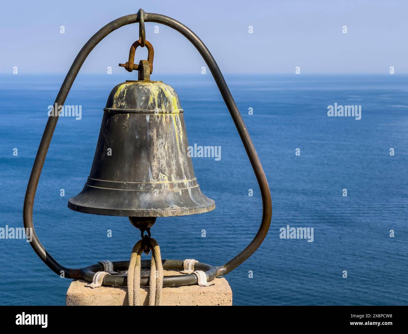 Cattura l'essenza della storia marinara con questa splendida immagine con una campana di bronzo invecchiata sullo sfondo tranquillo dell'oceano. Foto Stock