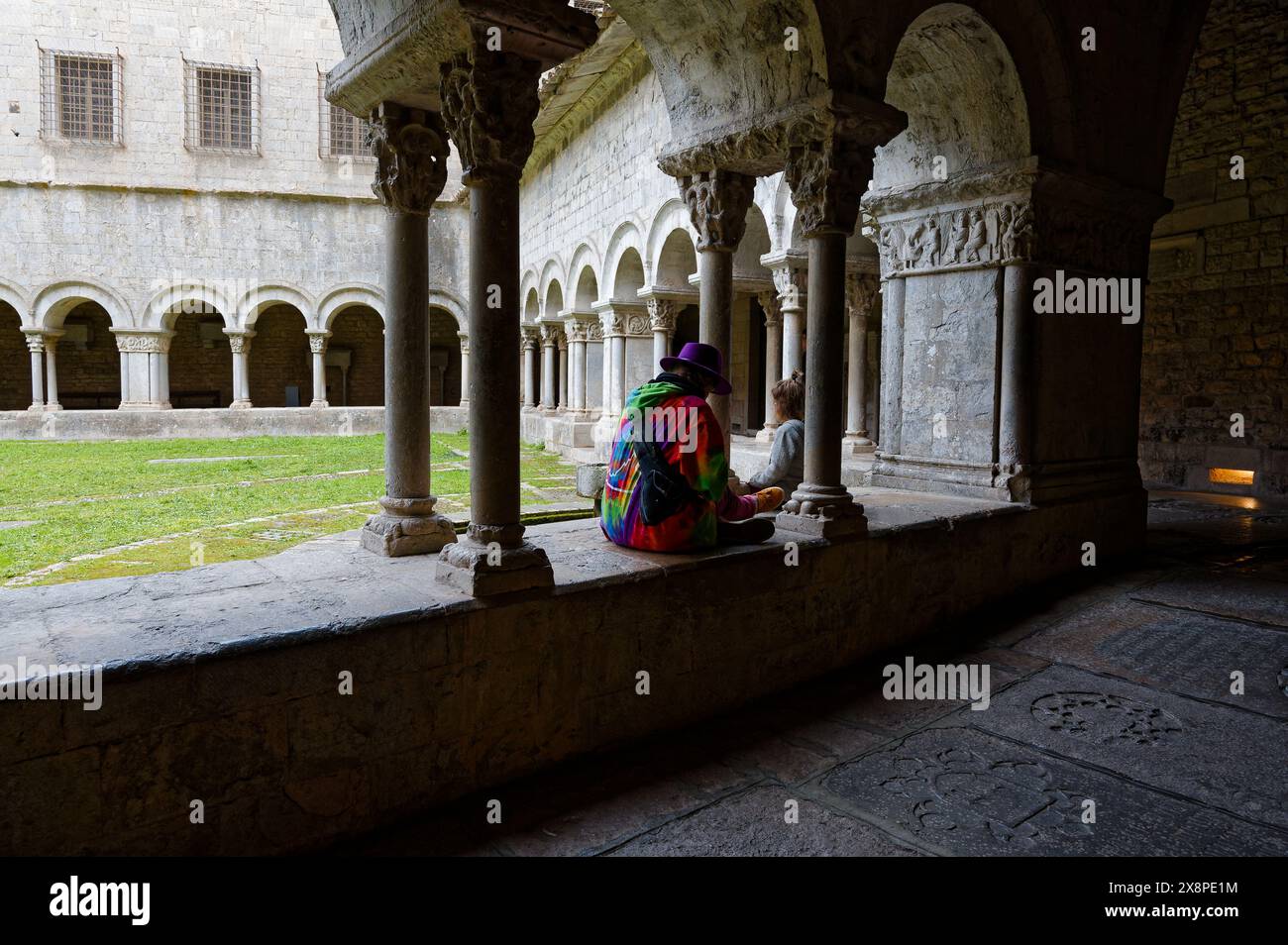 Felpa con cappuccio tie-dye e cappello viola che indossa la madre con la figlia siedono nel chiostro romantico della cattedrale di Santa Maria a Girona. Foto Stock