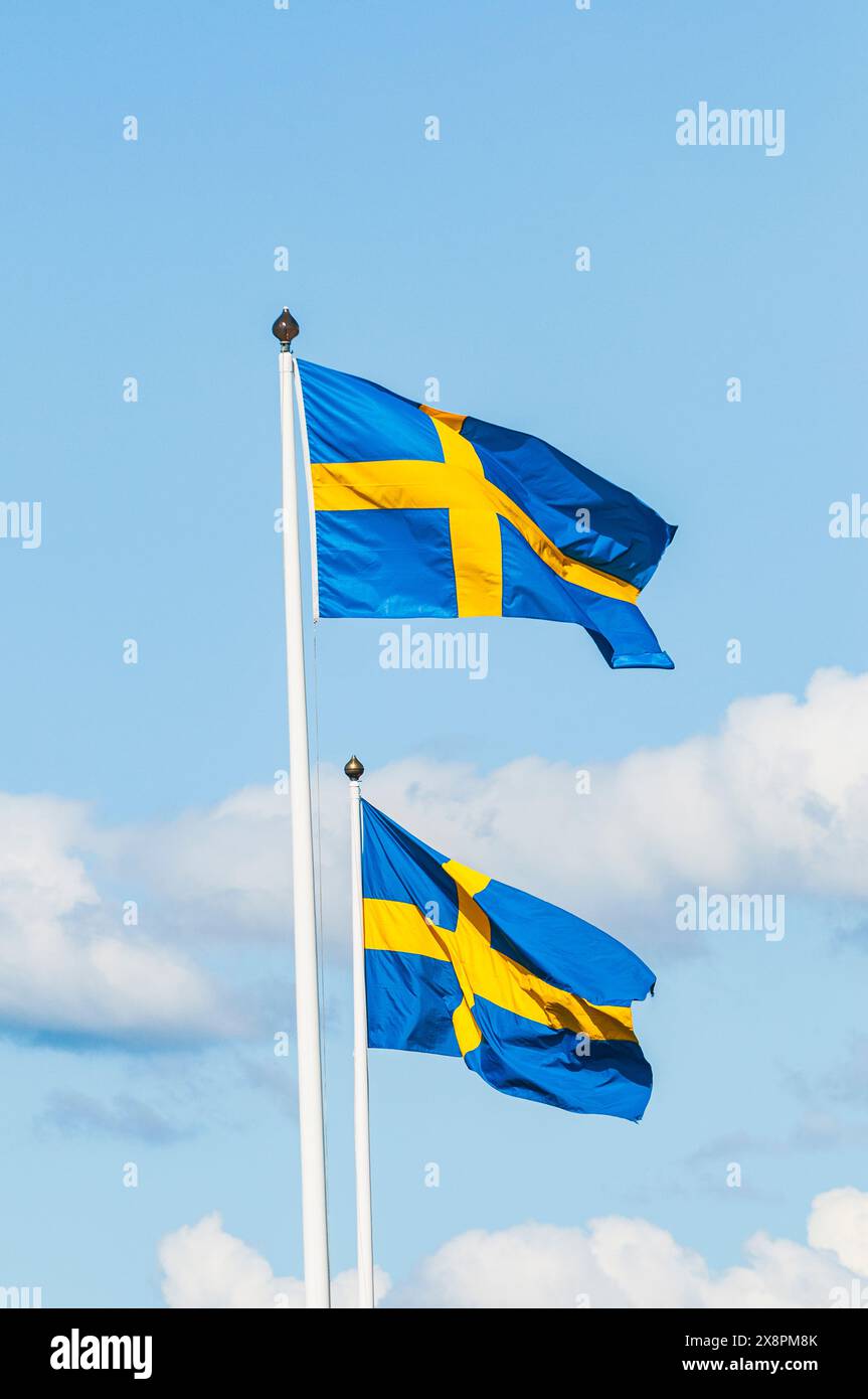Due bandiere svedesi sventolano nella brezza in una giornata di sole, creando un'esposizione patriottica contro il cielo blu. Foto Stock