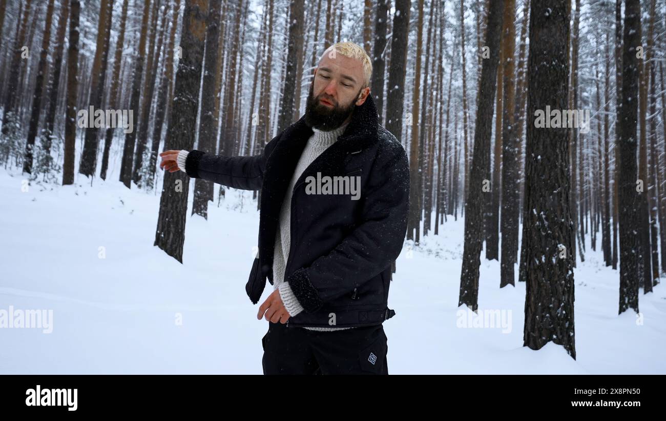 Ritratto di un bel giovane barbuto in abiti caldi in piedi all'aperto nel parco il giorno invernale. Supporto. Modello biondo hipster nei legni. Foto Stock