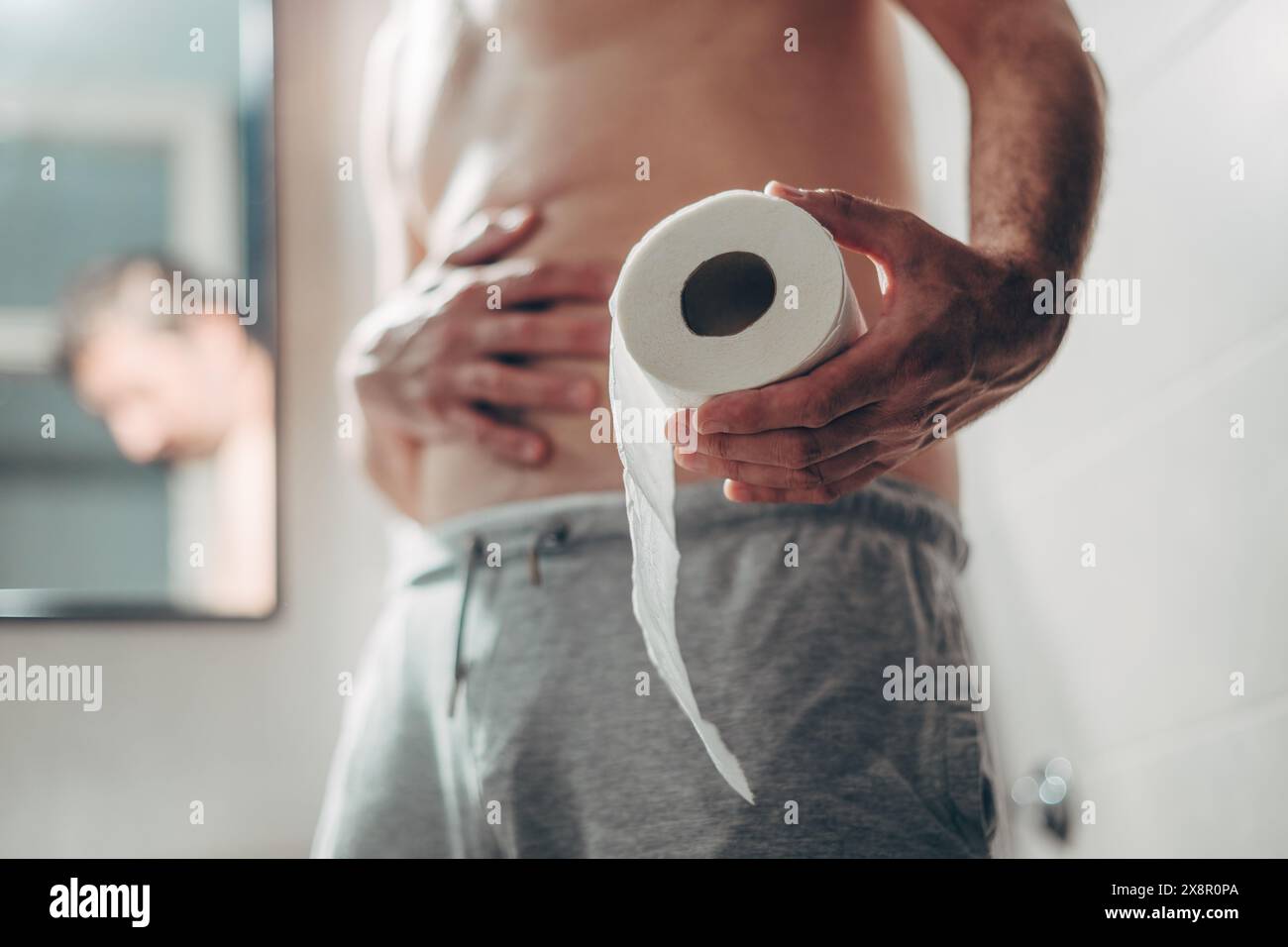 Concetto di costipazione, uomo adulto maturo stipato in piedi in bagno con rotolo di carta igienica, messa a fuoco selettiva Foto Stock