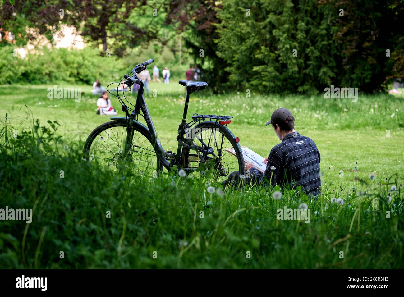 Ein Student sitzt neben seinem Fahrrad im Park an der ILM und zeichnet. Veröffentlichungen nur für redaktionelle Zwecke. Foto: IMAGO/FotoPrensa Foto Stock