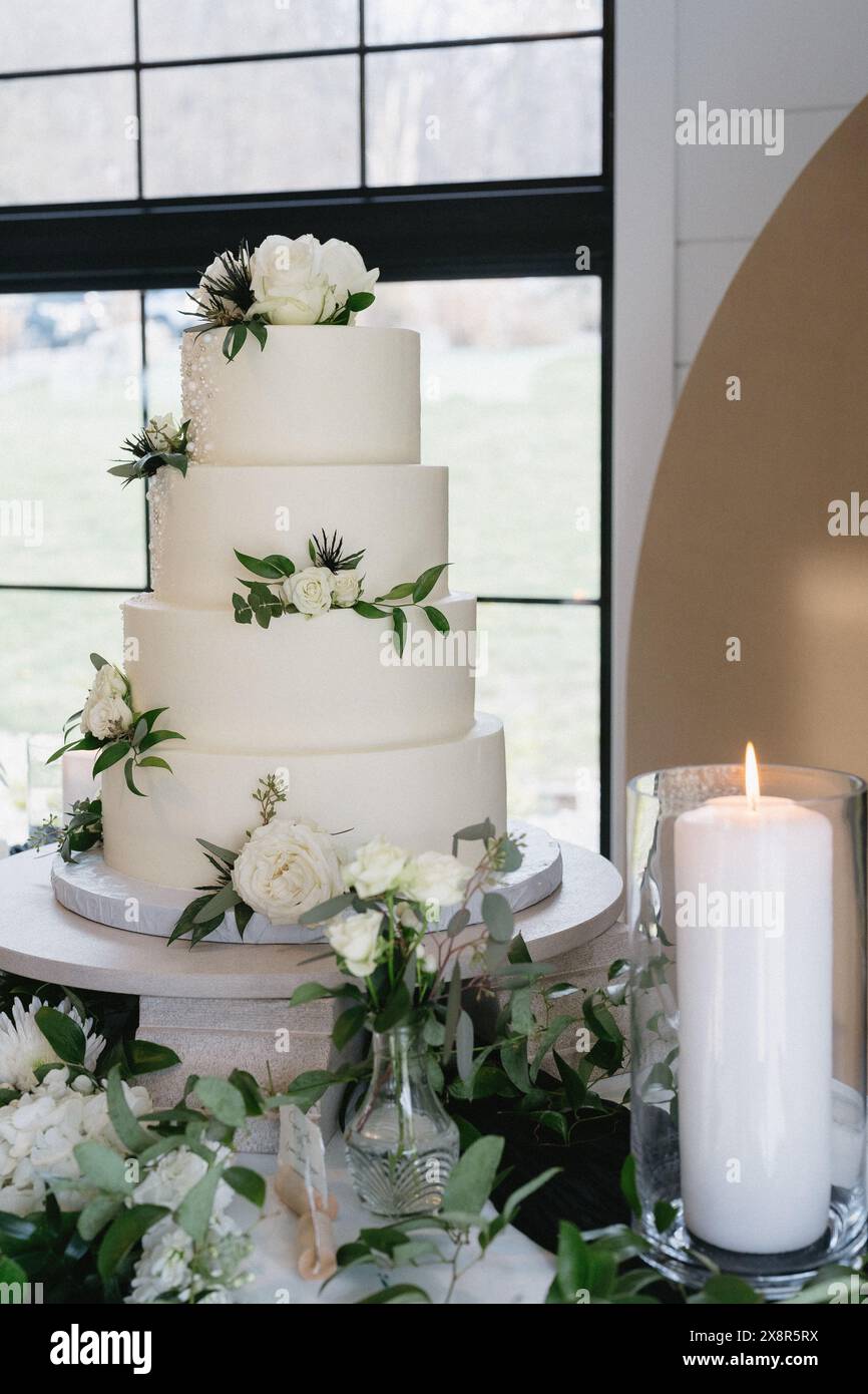 elegante torta nuziale a quattro piani con fiori bianchi e vegetazione Foto Stock