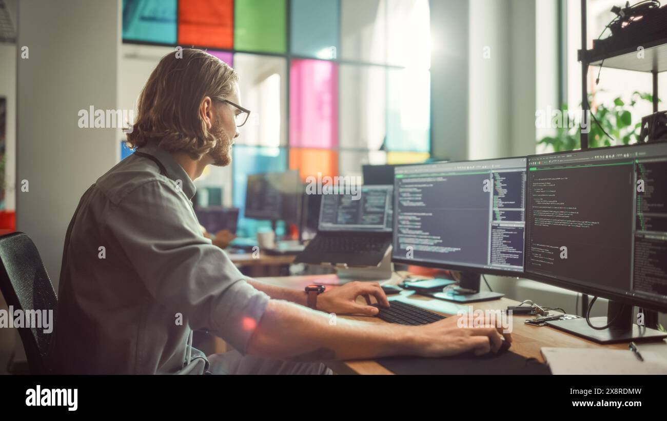 Programmatore maschio professionista che scrive codice su computer desktop con più display in elegante ufficio. Caucasian Man esegue lo scraping dei dati per una Start-up innovativa di intelligenza artificiale. Foto Stock
