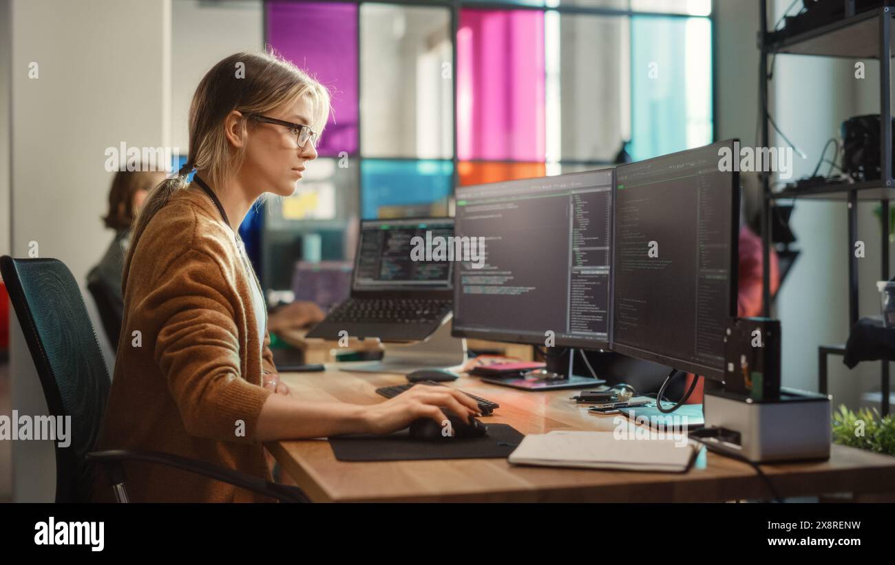 Codifica donna caucasica su PC desktop e laptop con più display in un ufficio spazioso. Junior software Engineer donna che lavora su New Sprint of Mobile Application Development for Start-Up. Foto Stock