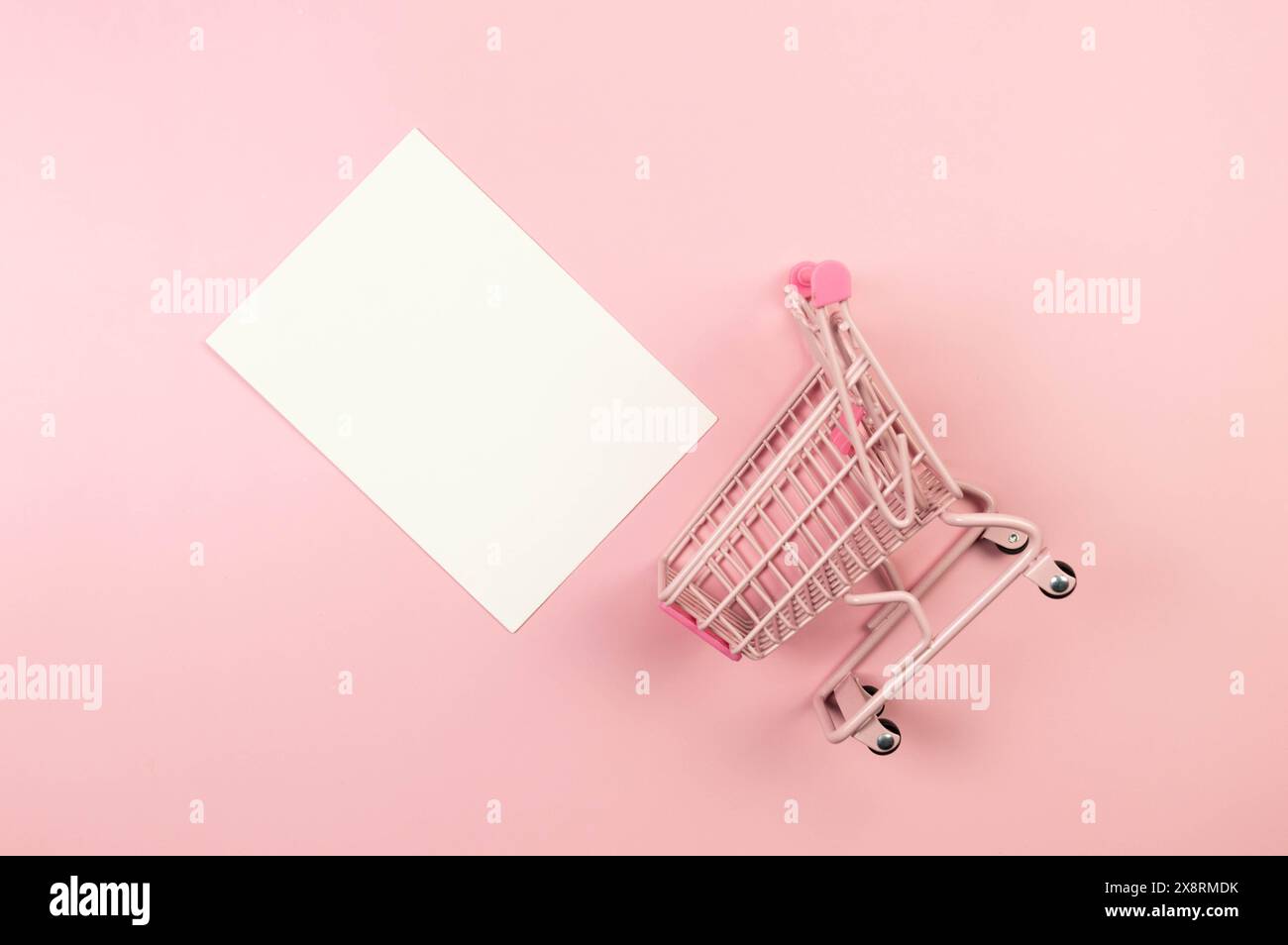 Vista dall'alto del carrello dello shopping rosa su sfondo rosa. Carta da parati per lo shopping creativa, carta bianca, vendita. Copia spazio, disposizione piatta. Foto Stock