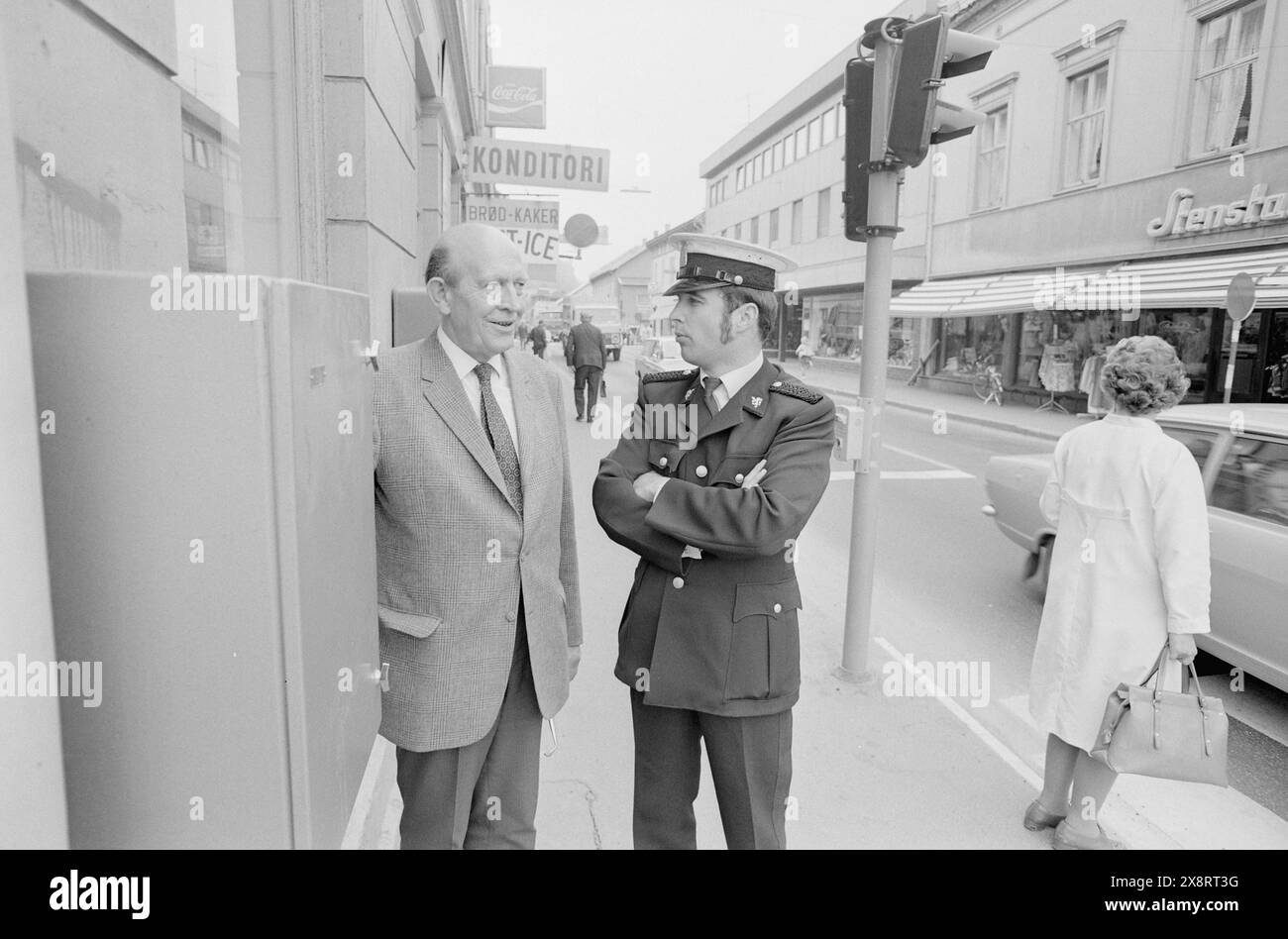 Aktuell 23-6-1973 : Byen som blir kvalt. Holmestrand en sommerdag: 17 000 biler giennom sentrum. Nå orker ikke folk mer støy, eksos og støv. E 18 Mà legges om dersom byen skal ha sianse til å overleve. I over tjue år har innbyggerne i denne idyliske lille kystbyen i Vestfold arbeidet for å få lagt sørlandske hovedvei — e 18 - utenom byen. Stasjonssjef Johnny Smith og politikonstabel Hans Ettersteen tester trafikklyset, som har gjort det mulig å krysse e 18. Foto: Aage Storløkken/Aktuell/NTB **FOTO IKKE BILDEBEHANDLET*** il testo dell'immagine è tradotto automaticamente Foto Stock