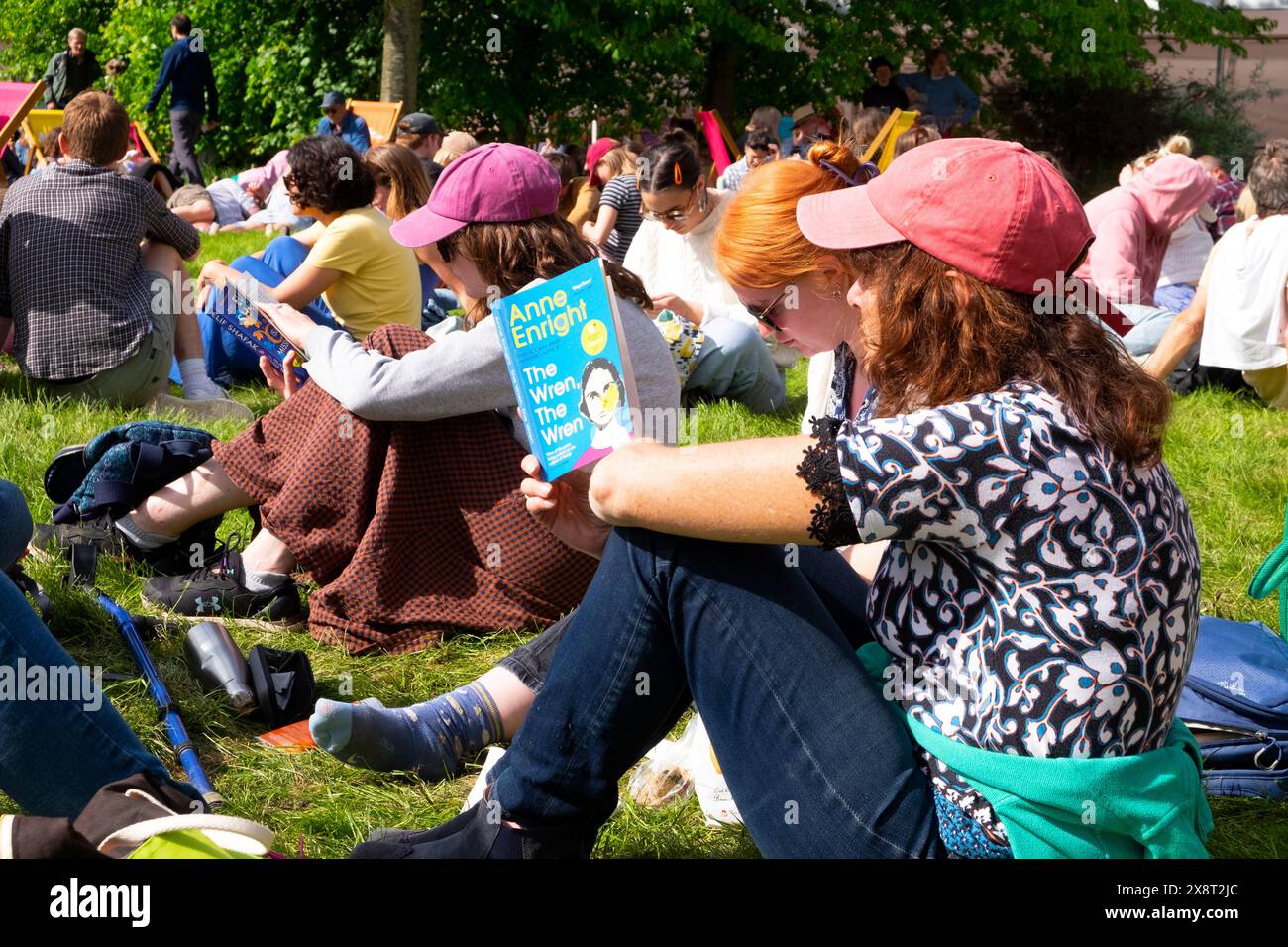 Donne visitatori persone sedute sul prato fuori dalla libreria Hay Festival che leggono libri rilassanti sotto il sole 2024 Wales UK Great Brighton KATHY DEWITT Foto Stock