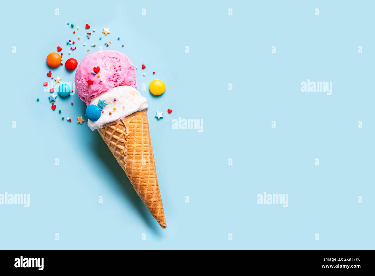 Una tazza di gelato alla vaniglia e alle fragole in un cono di cialda decorato con spolverini di zucchero su sfondo blu, copia spazio. Layout creativo alla moda di ICE c Foto Stock