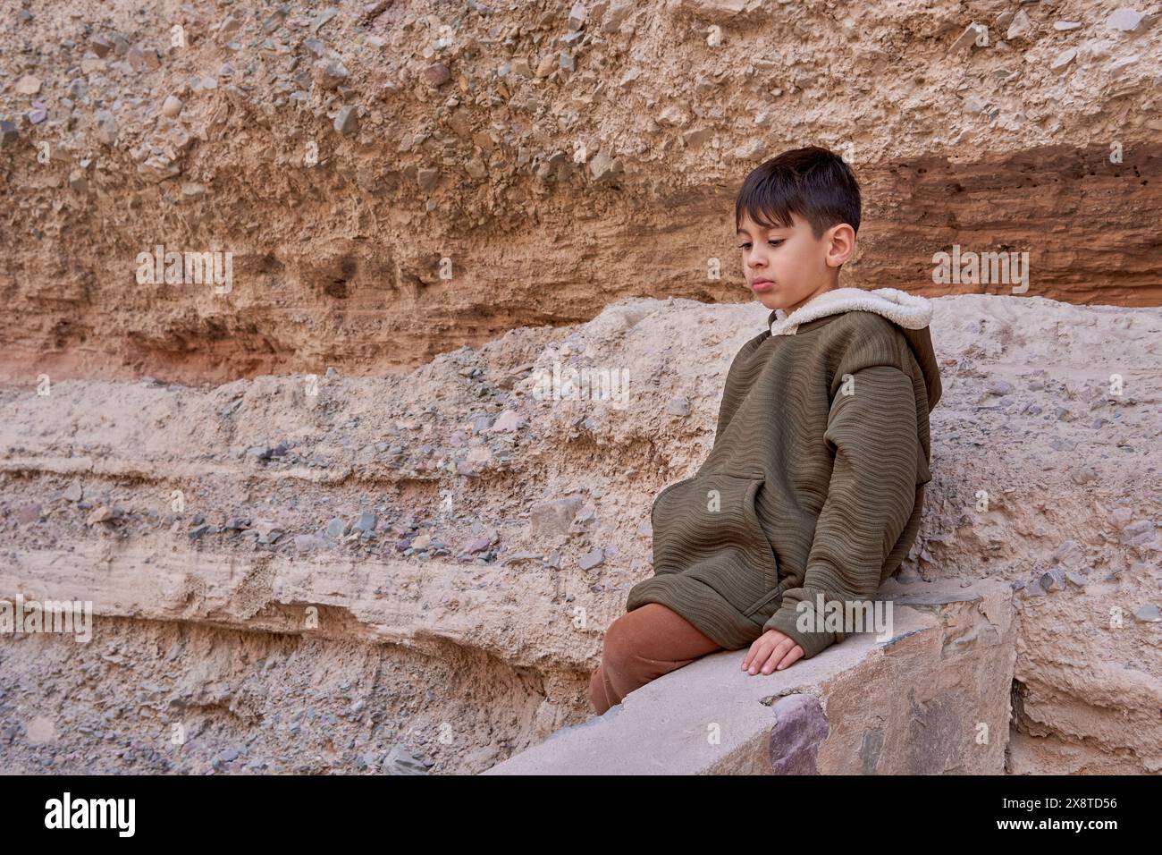 Ragazzo latino seduto su una roccia che guarda in basso stanco dopo un'escursione a Iruya, Salta Foto Stock