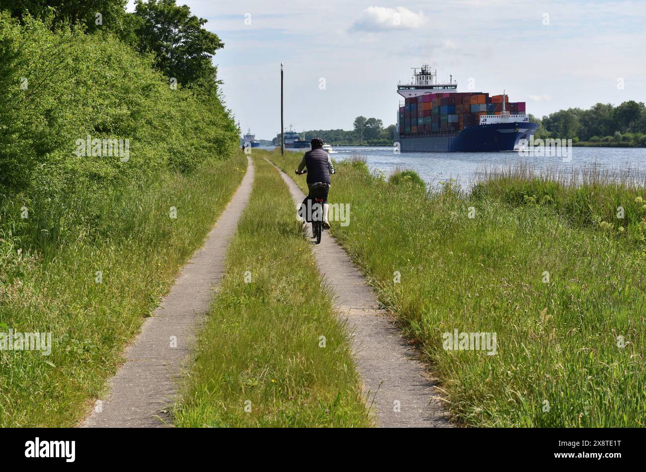 In bicicletta con una nave portacontainer sul canale di Kiel, Kiel, Schleswig-Holstein, Germania Foto Stock