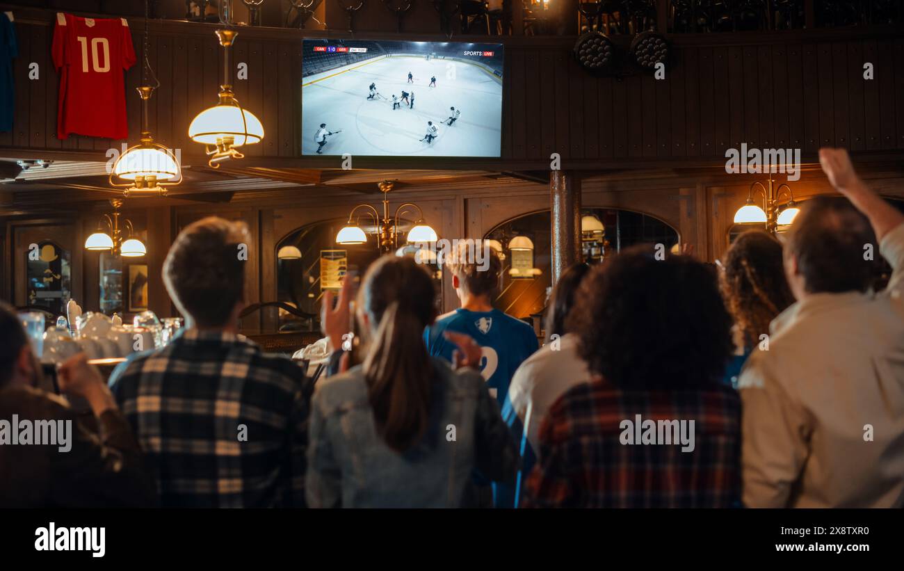 Gruppo di fan di hockey su ghiaccio che guardano una partita dal vivo trasmessa in TV in un pub sportivo. Le persone esultano, sostengono la loro squadra. La folla diventa entusiasta quando la squadra segna un gol e vince il campionato. Foto Stock