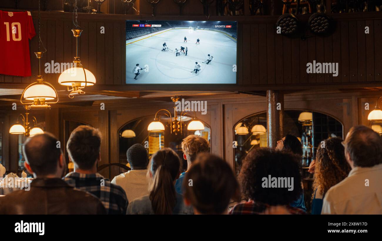 Gruppo di fan di hockey su ghiaccio che guardano una partita dal vivo trasmessa in TV in un pub sportivo. Le persone esultano, sostengono la loro squadra. La folla diventa entusiasta quando la squadra segna un gol e vince il campionato. Foto Stock