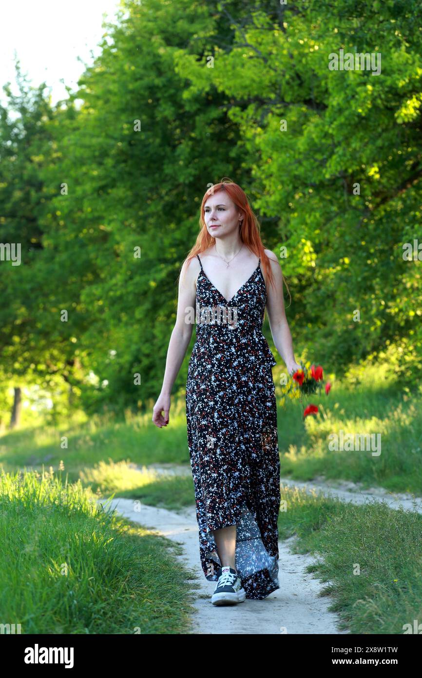 Una ragazza con papaveri selvatici gode della vista da una collina vicino al fiume. Gioia, felicità, serenità. Papaveri selvatici vicino al fiume. Foto Stock