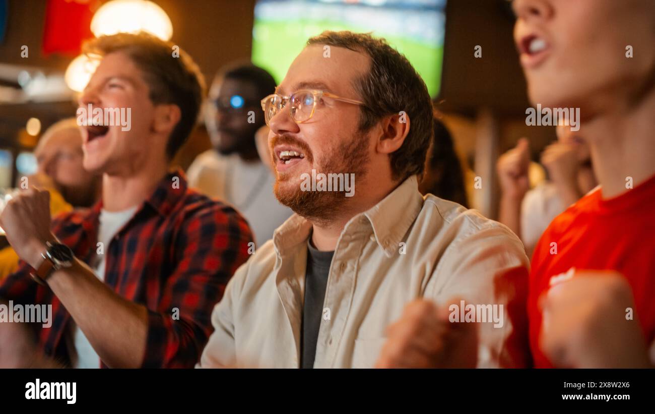 Gruppo di amici che guardano una partita di calcio dal vivo in TV in un bar dello sport. Tifosi contenti che bramano e urlano. I giovani festeggiano quando la squadra segna un gol e vince la Coppa del mondo di calcio. Movimento lento. Foto Stock