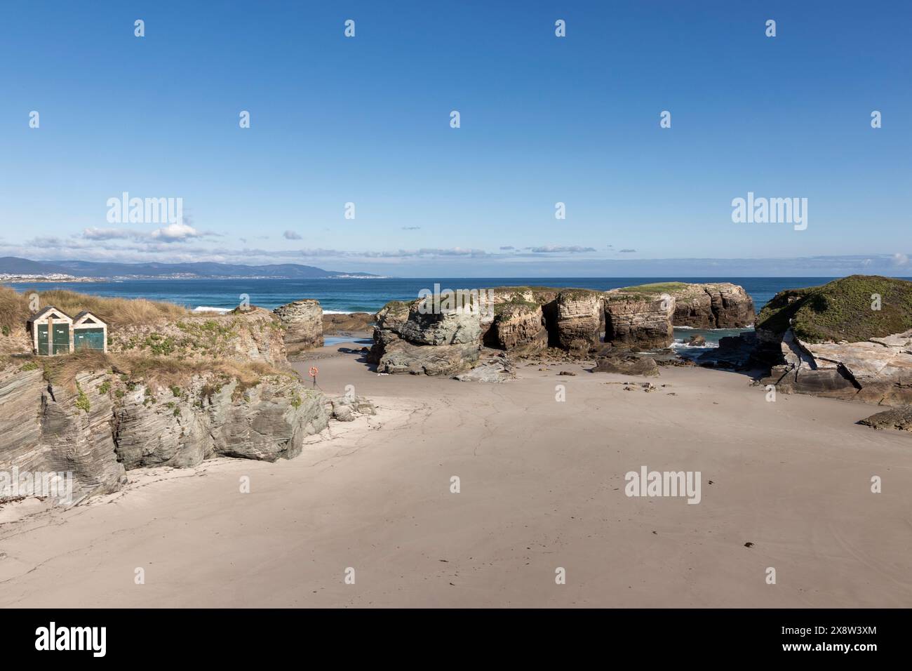 paesaggio costiero con spiaggia sabbiosa, formazioni rocciose, cielo limpido e corpo d'acqua distante Foto Stock