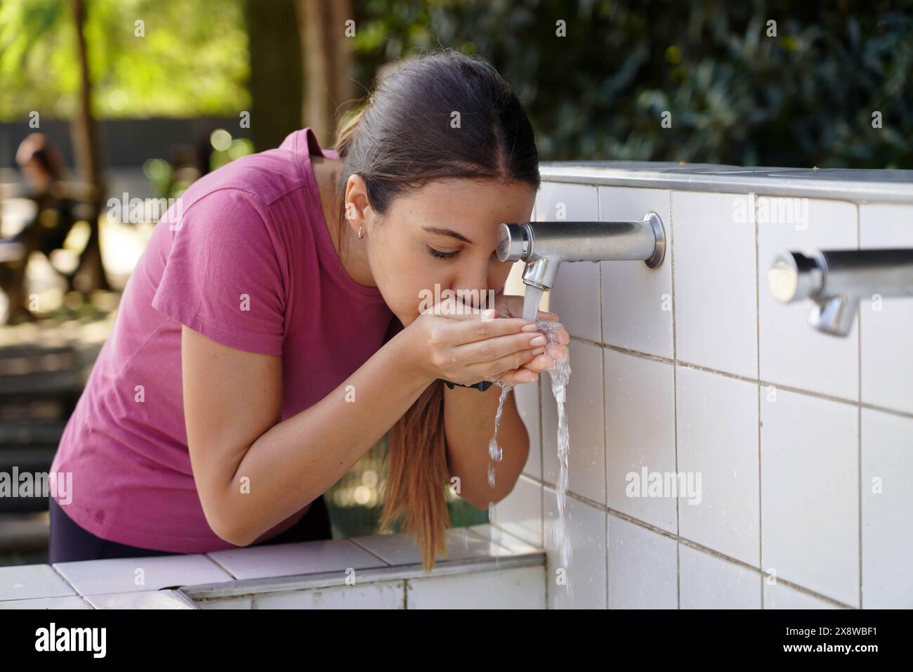 Il primo piano di una giovane donna si reidrata con l'acqua di una fontana nel parco pubblico Foto Stock