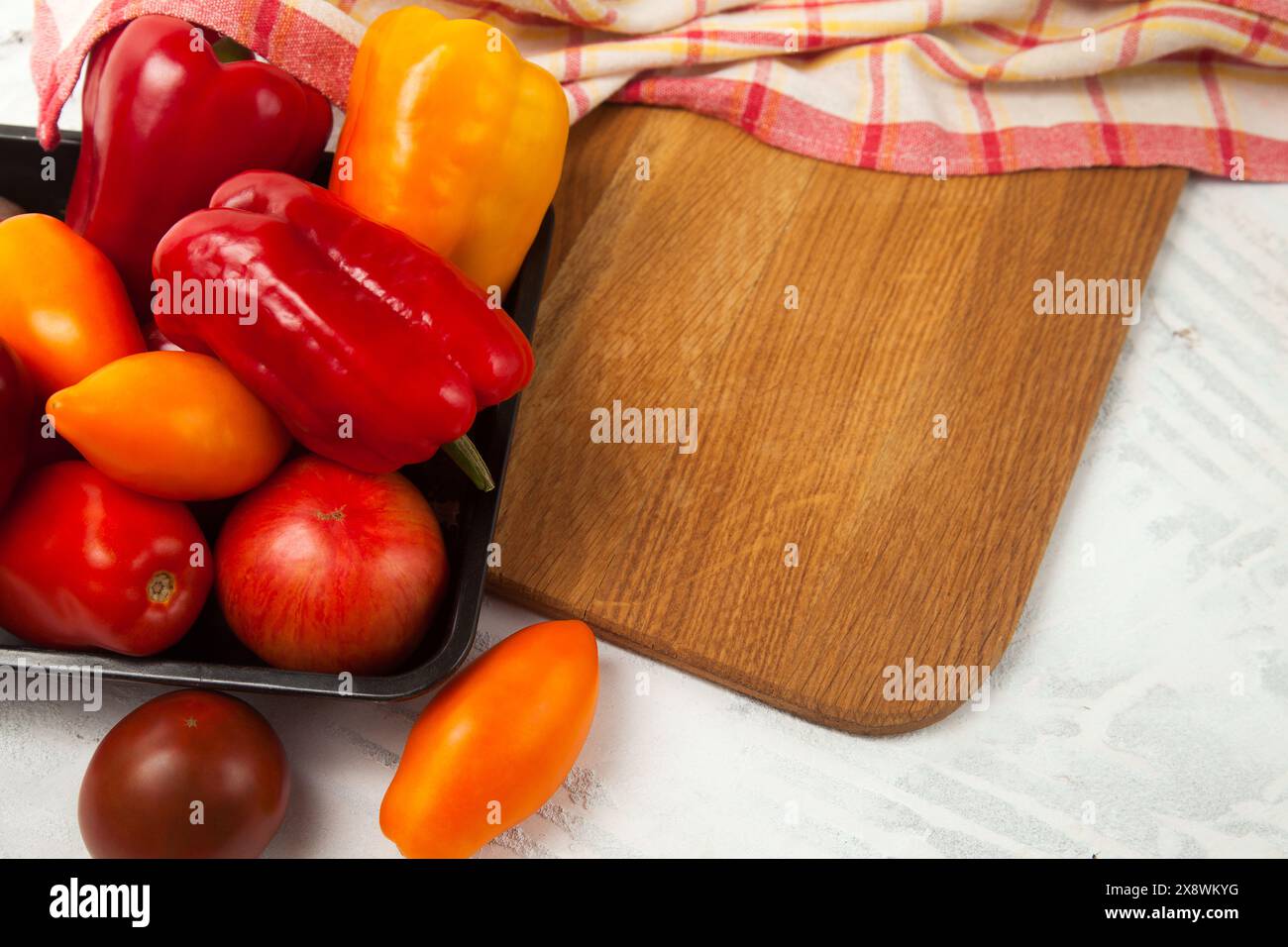Immagine di sfondo vegetale. Ciotola con verdure su tagliere con assort di diversi pomodori succosi interi e peperoni su una b di legno bianco Foto Stock