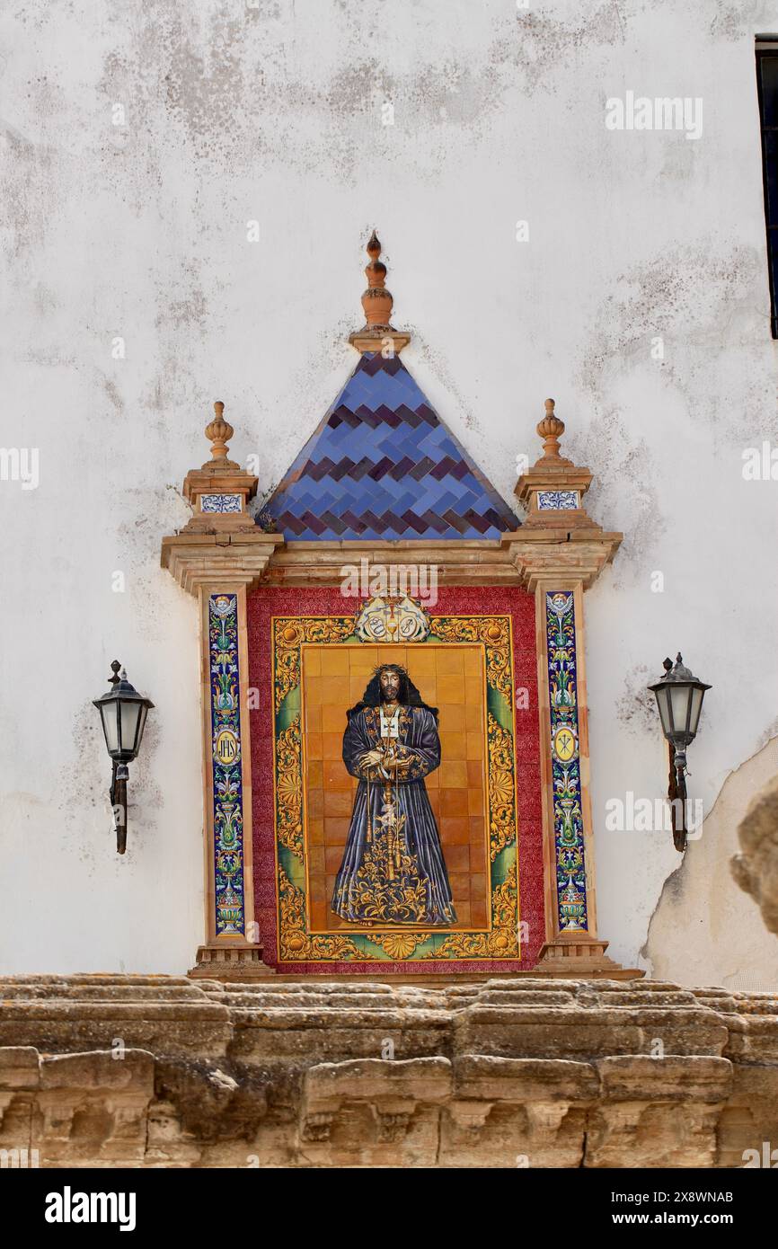 Un colorato e ornato murale di un santo sulla facciata di un edificio, fiancheggiato da due lanterne, che mostra l'arte religiosa spagnola tradizionale Foto Stock