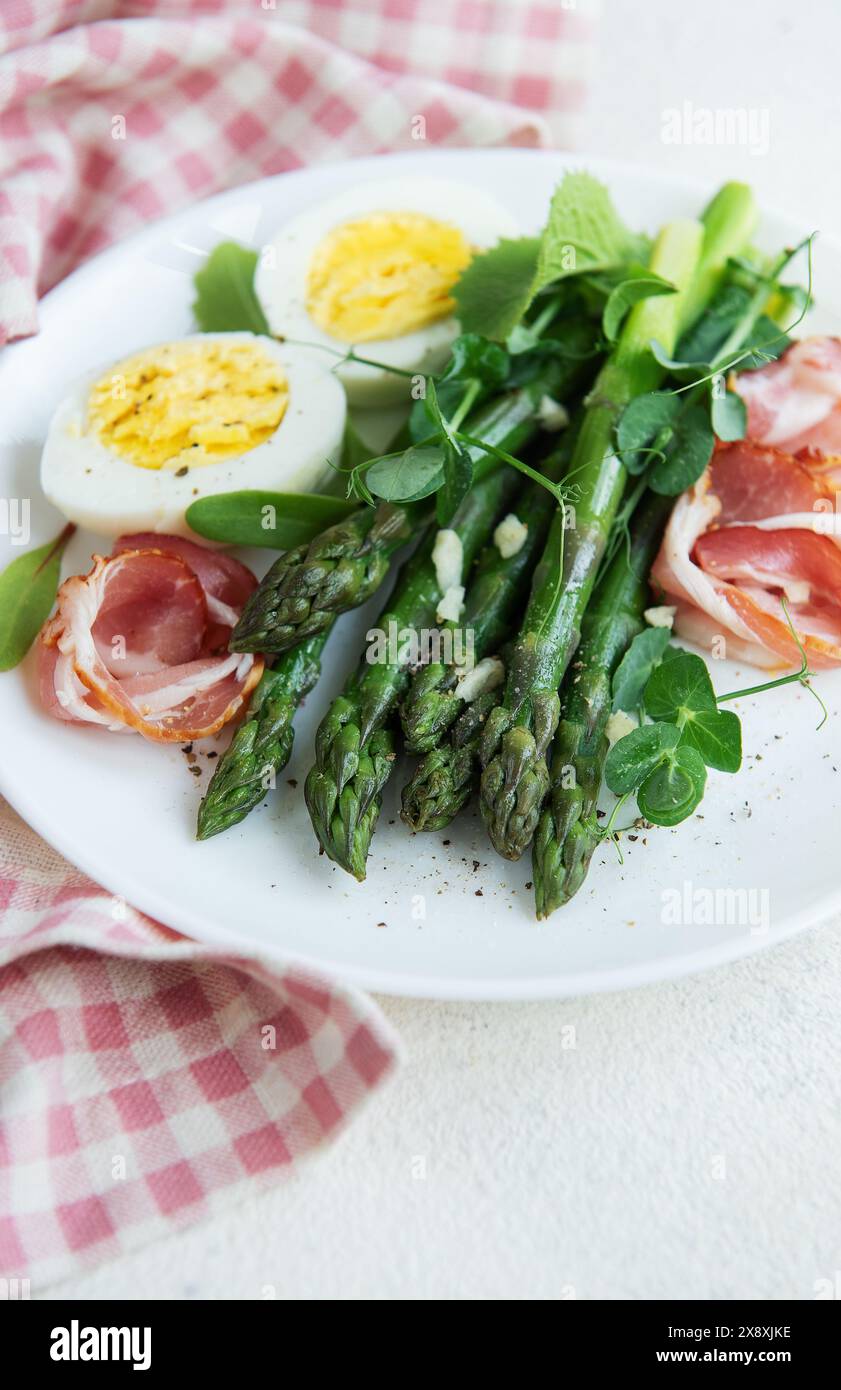 Un'insalata salutare composta da lance di asparagi verdi, prosciutto a fette sottili e metà di un uovo sodo, guarnite con foglie di microverdure fresche, Foto Stock