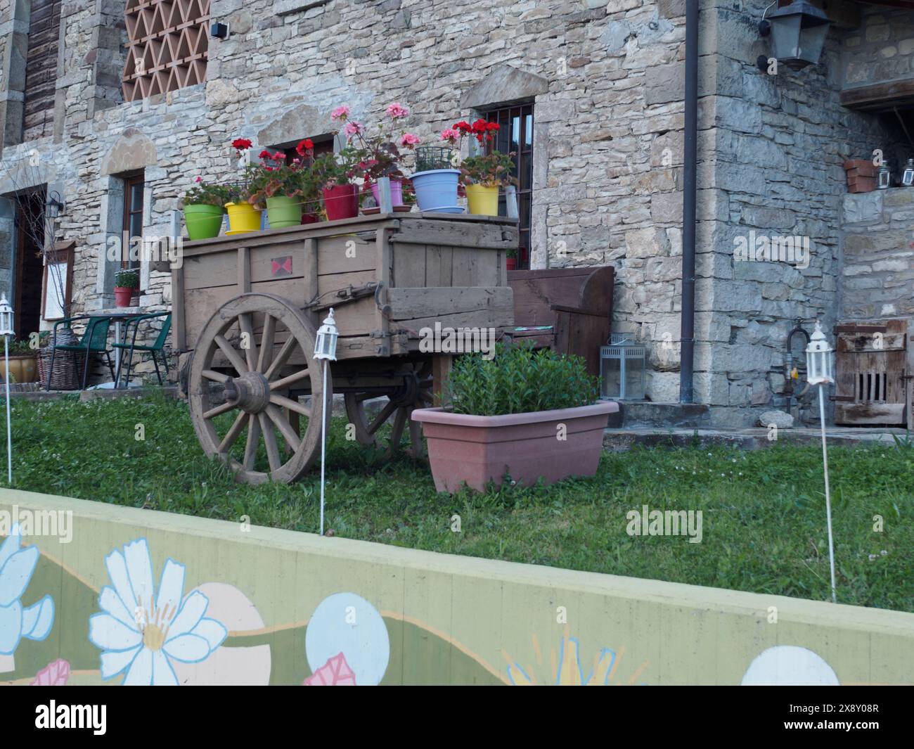 Morfasso , Italia - 15 maggio 2024 carrello in legno d'epoca adornato con vasi di fiori colorati di fronte ad un edificio in pietra, che incarna il fascino rurale e la pastora Foto Stock