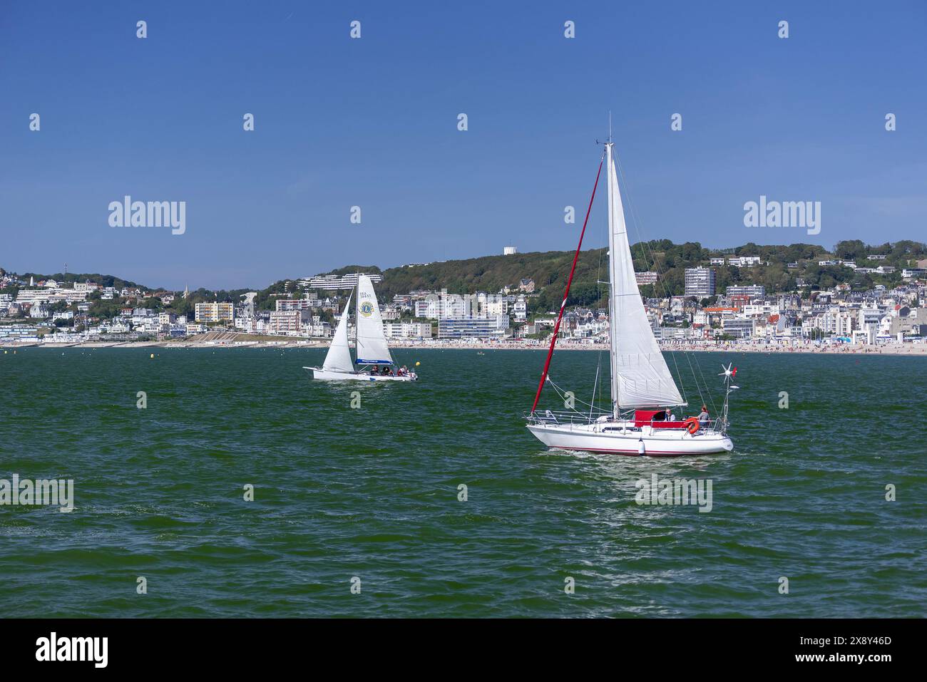 Le Havre, Francia - Vista su piccole barche a vela che navigano nel Canale della Manica con la città di le Havre e la sua spiaggia di ciottoli sullo sfondo. Foto Stock