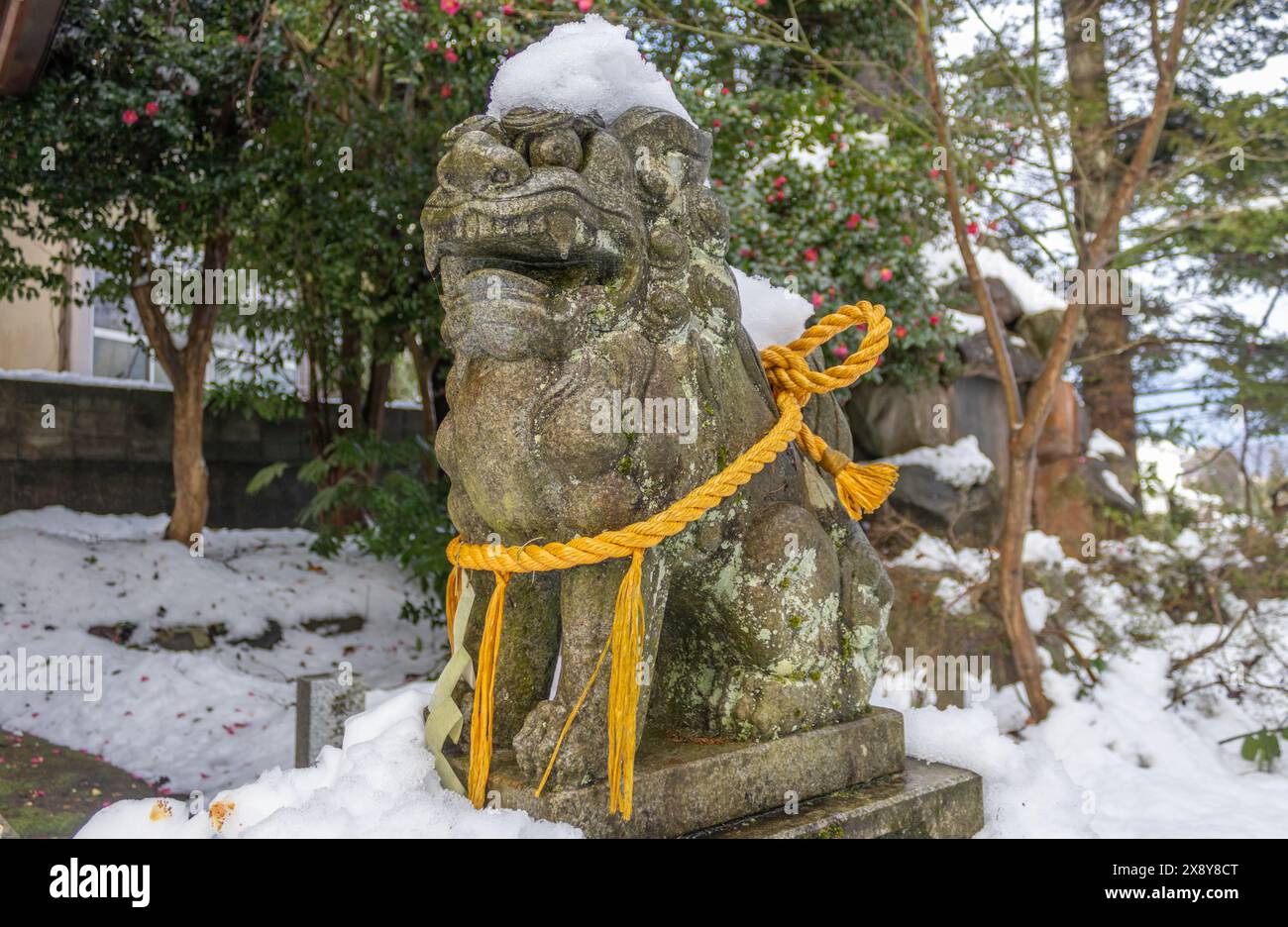 Statua di komainu, o cane da leone, nella neve invernale con corda sacra di shimenawa nel piccolo santuario locale, Kanazawa, Giappone. Foto Stock