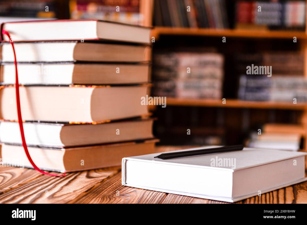 Un quaderno bianco e una matita nera sul desktop con scaffali sullo sfondo della libreria. Libri Foto Stock