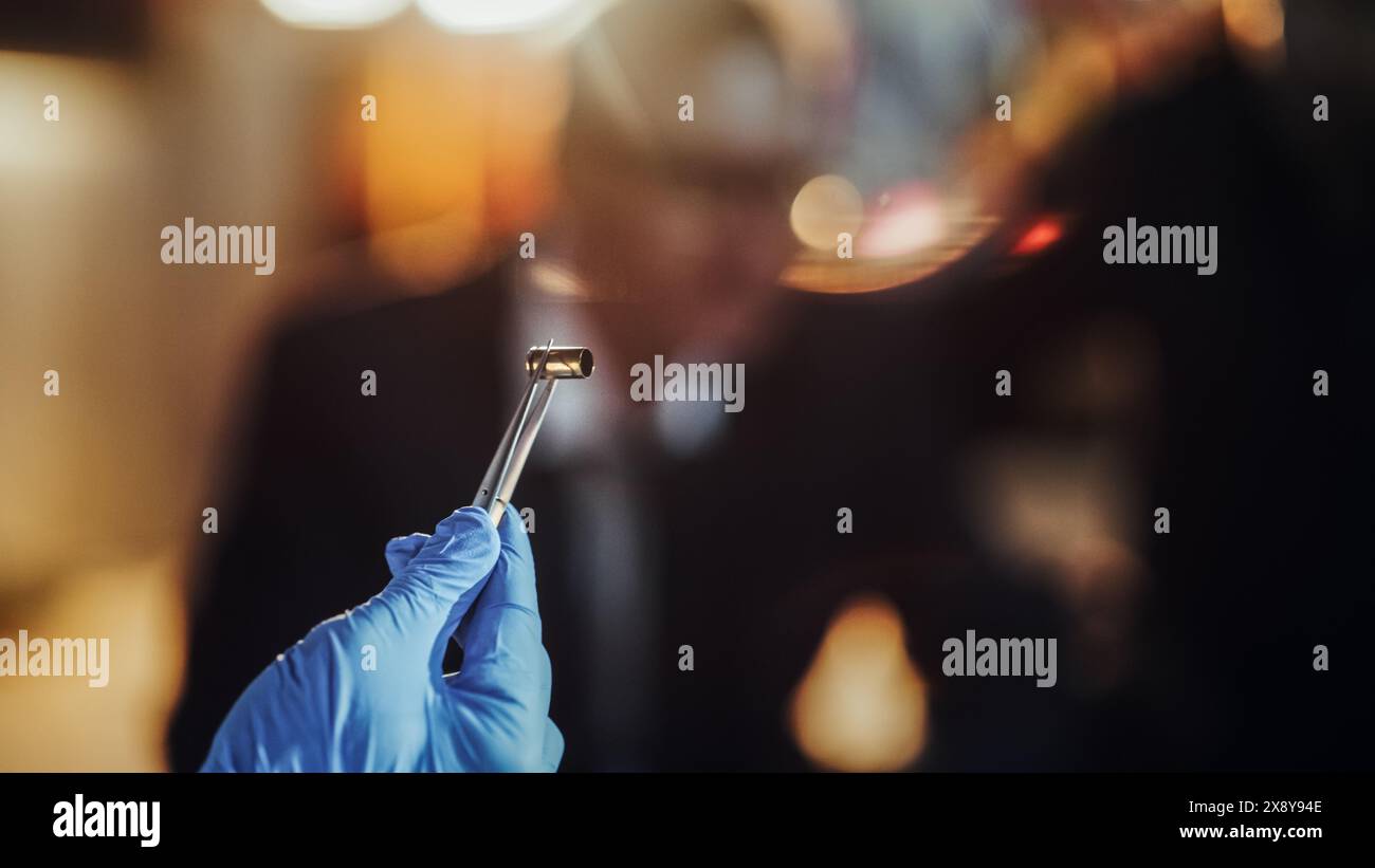 Primo piano estremo con sfondo sfocato: Mano con guanto medico utilizzando pinzette per tenere un guscio proiettile. Specialista forense che trova la cartuccia sulla scena del crimine e la mostra al detective come prova Foto Stock