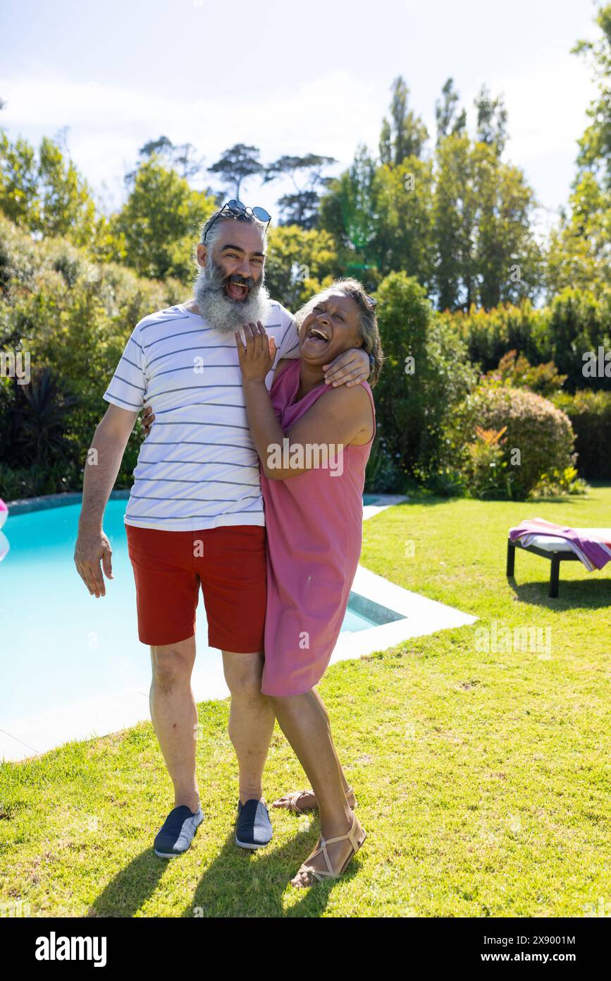 All'aperto, diversi amici anziani, ridendo vicino alla piscina, indossando abiti estivi informali Foto Stock