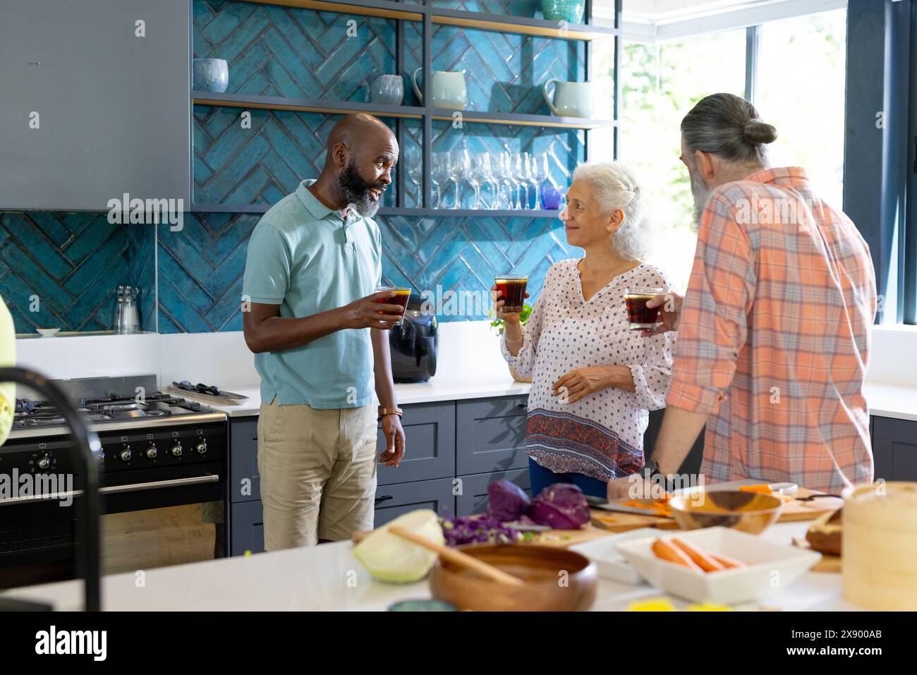 Amici anziani diversi che si godono un drink a casa, discutono durante la preparazione dei pasti Foto Stock