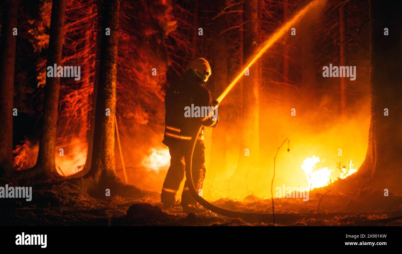 Elite Firefighter estinguendo metodicamente un grande incendio boschivo con acqua ad alta pressione proveniente da Firehose. Brigata dei vigili del fuoco che salva Wildland da incendi dolosi incontrollabili. Foto Stock