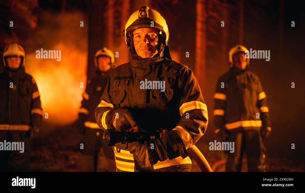 Squadra maschile e femminile di vigili del fuoco professionisti in piedi in una foresta fumata durante un incendio nel deserto, in posa e guardando la telecamera. Gruppo che indossa indumenti protettivi, caschi e altri articoli. Foto Stock