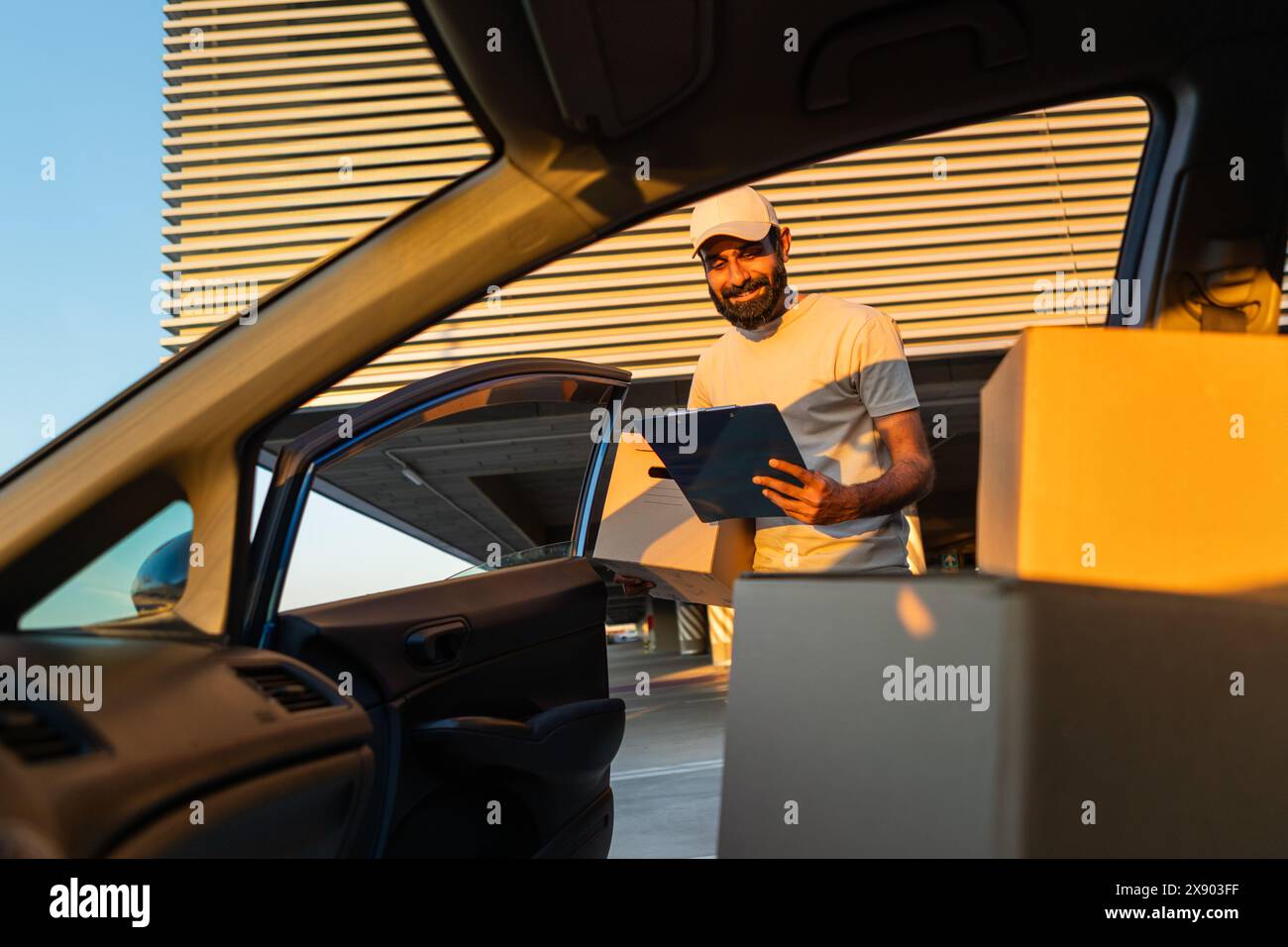 Il lavoratore addetto alle consegne scarica le scatole dall'auto all'edificio durante il tramonto Foto Stock