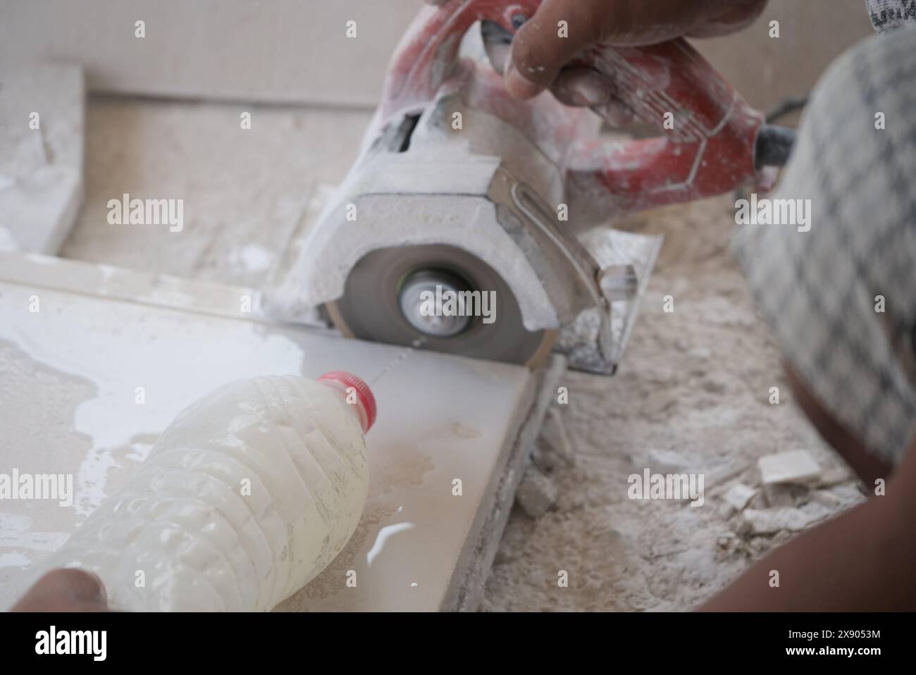 Un primo piano dettagliato cattura un artigiano esperto utilizzando una sega elettrica portatile per tagliare con precisione una piastrella, con polvere e detriti sparsi intorno. L'attenzione Foto Stock