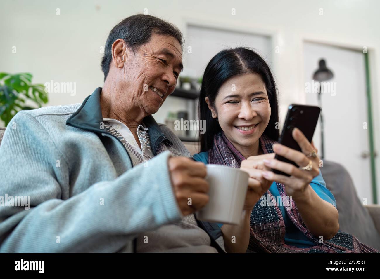 Anziani coppie sposate in pensione si rilassano insieme in soggiorno, utilizzando il cellulare Foto Stock