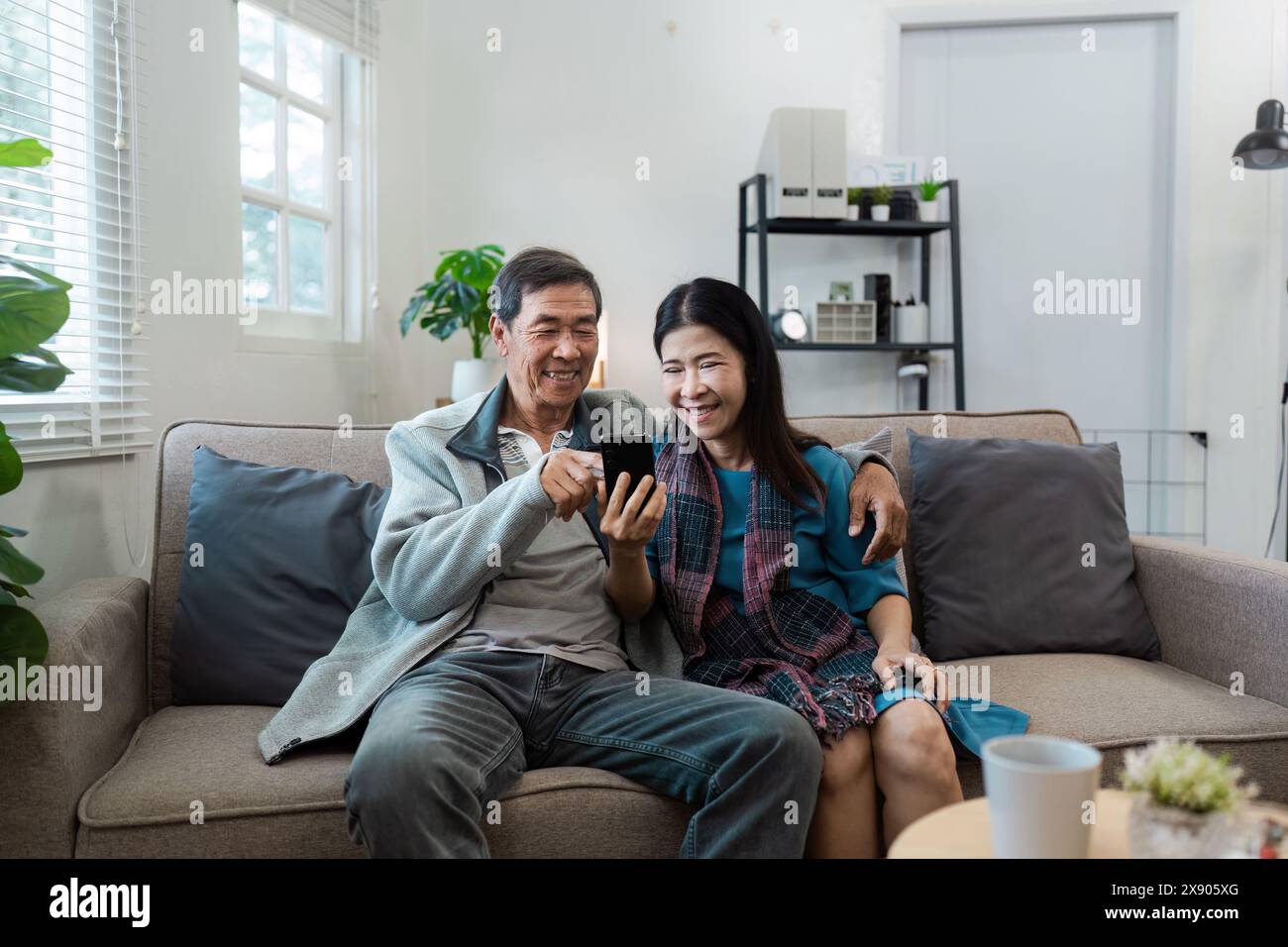 Anziani coppie sposate in pensione si rilassano insieme in soggiorno, utilizzando il cellulare Foto Stock