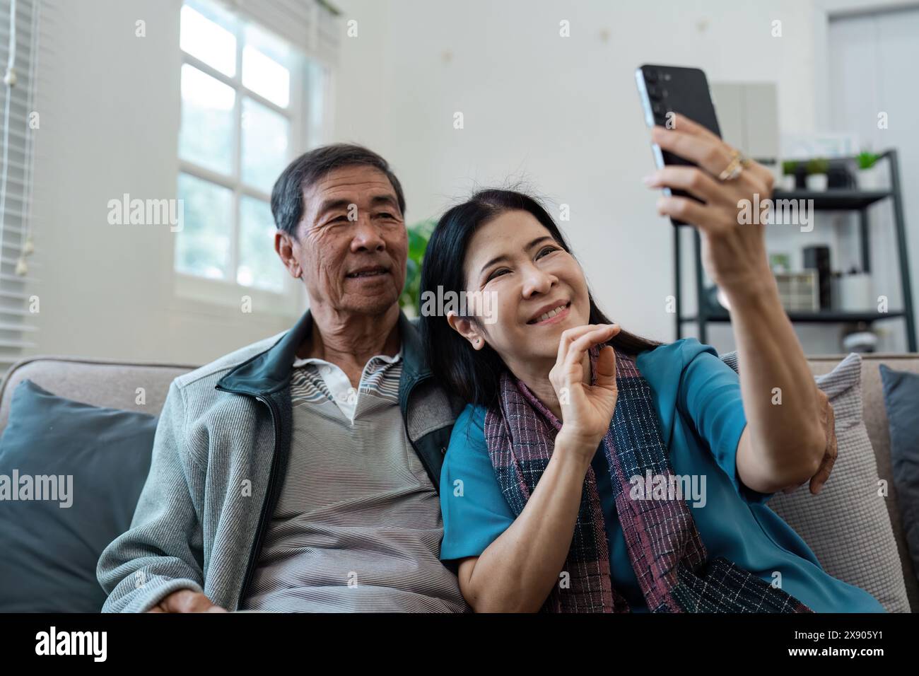 Anziani coppie sposate in pensione si rilassano insieme in soggiorno, utilizzando il cellulare Foto Stock