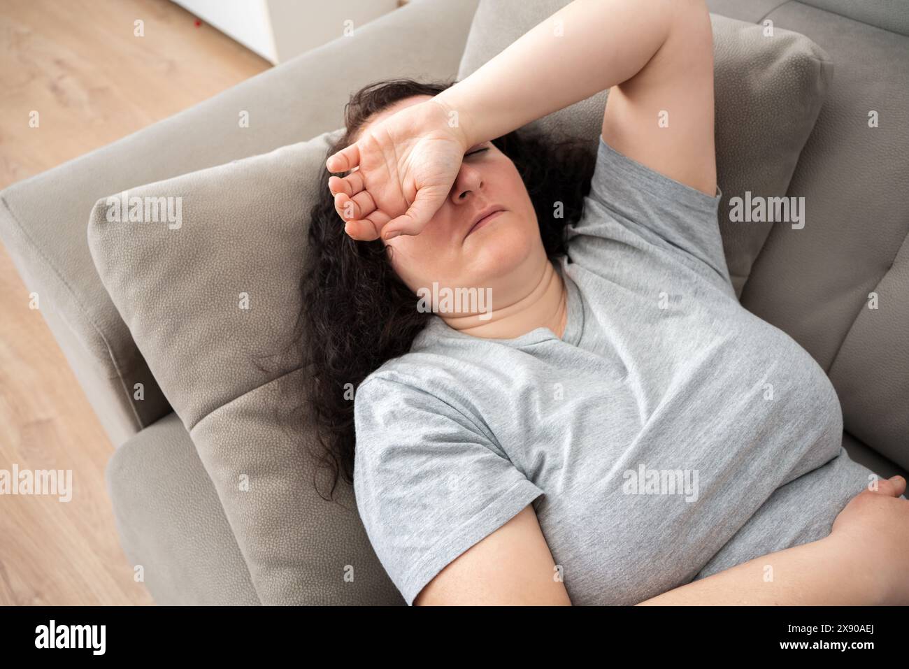 Donna tranquilla sdraiata sulla schiena sul comodo divano di casa, che copre gli occhi con le mani, dorme di giorno, si sente stanca, si gode il relax, il tempo libero, Foto Stock