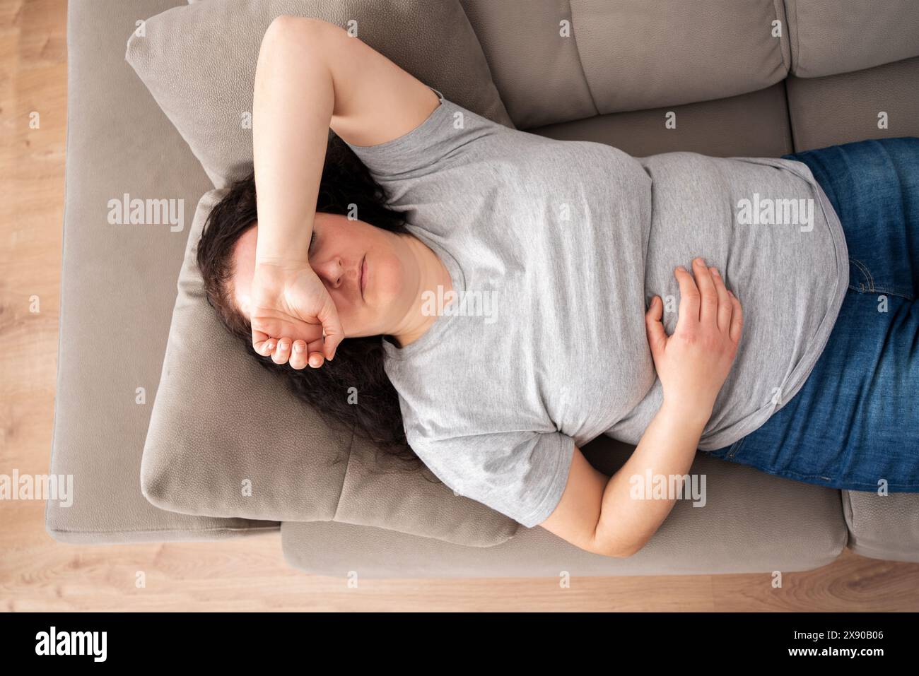 Donna tranquilla sdraiata sulla schiena sul comodo divano di casa, che copre gli occhi con le mani, dorme di giorno, si sente stanca, si gode il relax, il tempo libero, Foto Stock