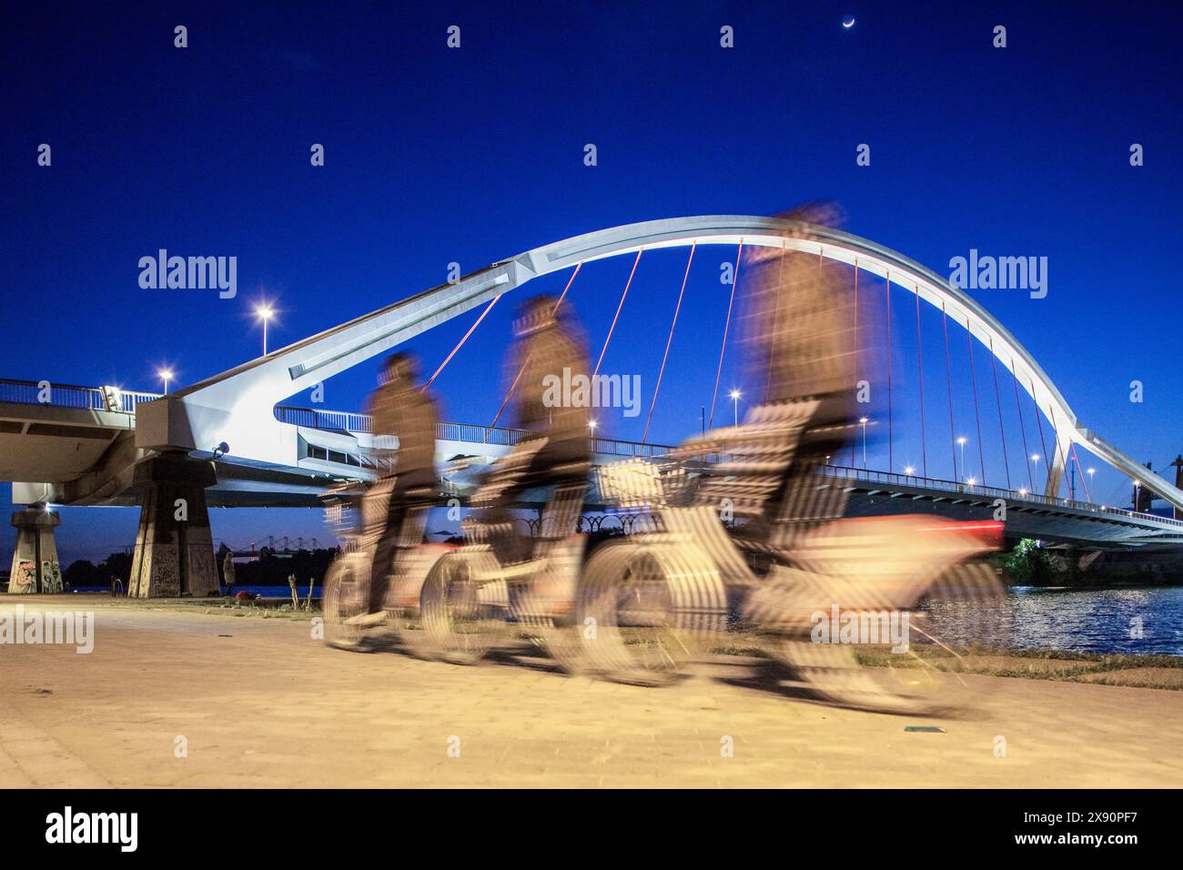 Un ciclista in movimento passa davanti al Ponte Barqueta illuminato a Siviglia di notte, catturato con una tripla esposizione artistica. Foto Stock