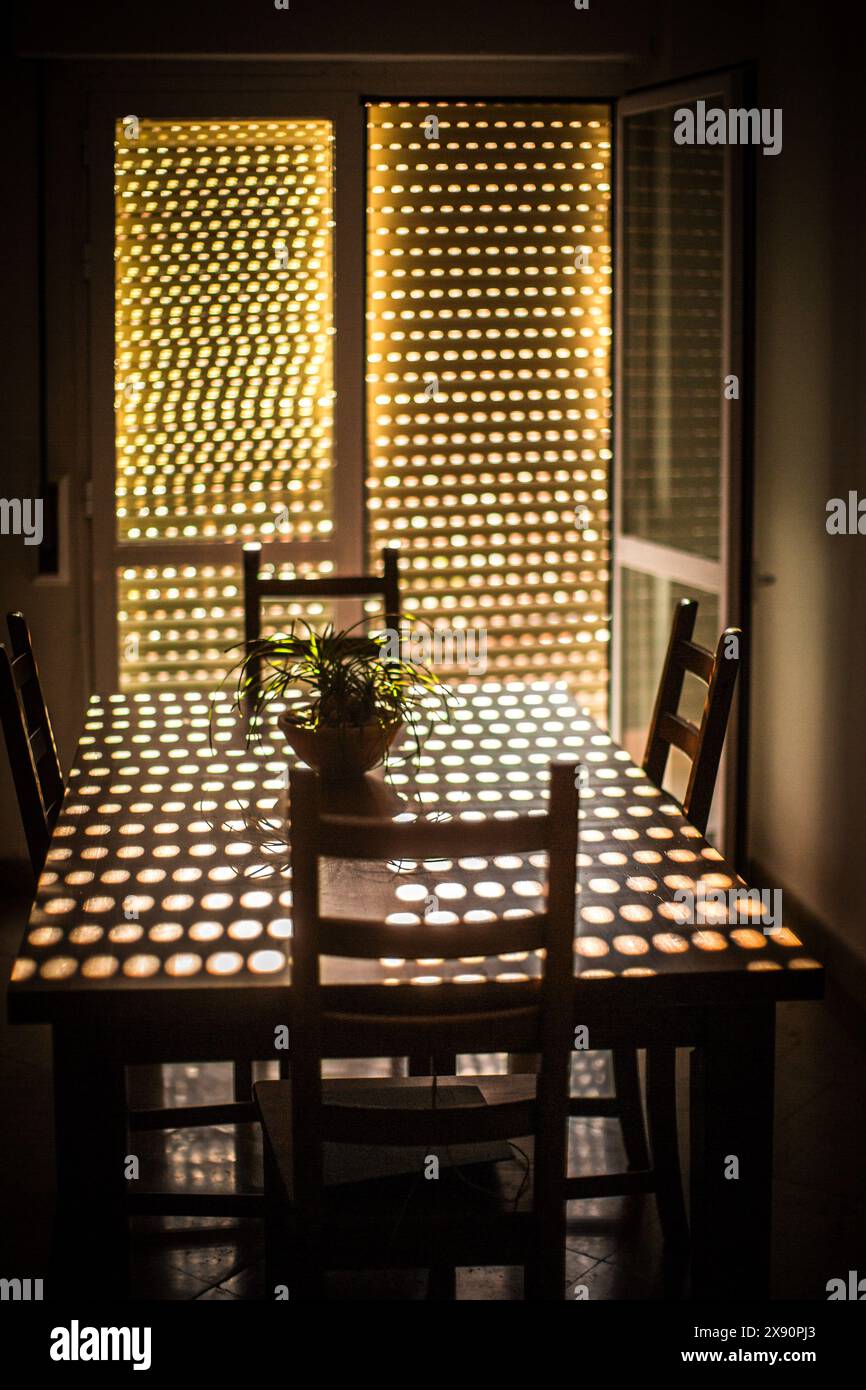 La luce del sole filtra attraverso le tonalità chiuse in una sala da pranzo, creando un effetto di luce a motivi geometrici sul tavolo e sulle sedie. Foto Stock