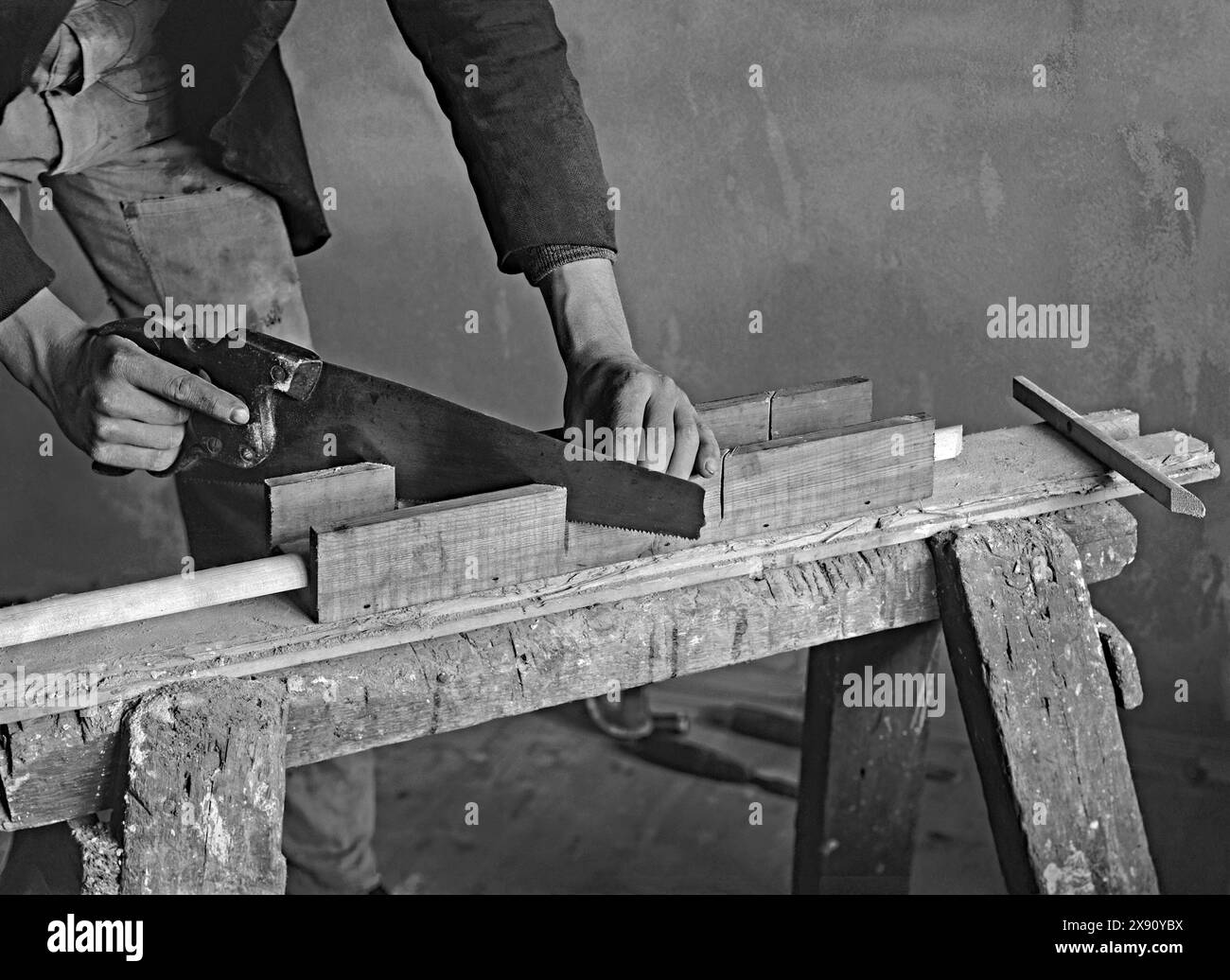 Un operaio edile che fa un taglio a 45 gradi in una striscia di legno con la sua sega utilizzando una scatola di legno. I lavori sono stati svolti in una casa a Kennel Lane, Fetcham, Leatherhead, Surrey, Inghilterra, Regno Unito c. 1930. La scatola aiutava a fare tagli a 45° e 90° ed era comunemente usata dagli anni '1800 Questo si appoggia su uno sgabello da falegname ben indossato/cavallo da sega o cavalletto - una fotografia vintage anni '1920/'30. Foto Stock