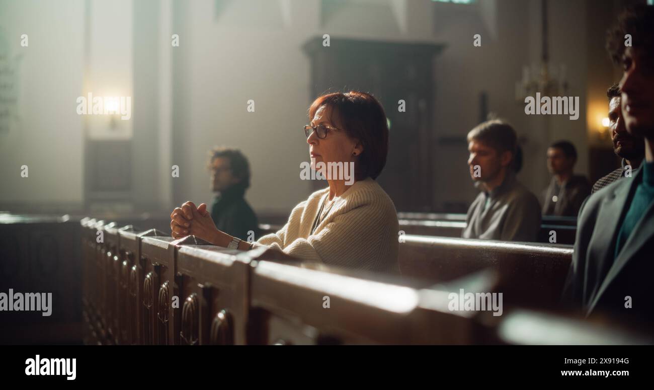 Gruppo di fedeli parrocchiani nella grande Vecchia Chiesa che ascoltano il sermone. Devota Signora cristiana con le mani piegate sta pregando. La gente cerca una guida morale dal Religios fait nel luogo sacro Foto Stock