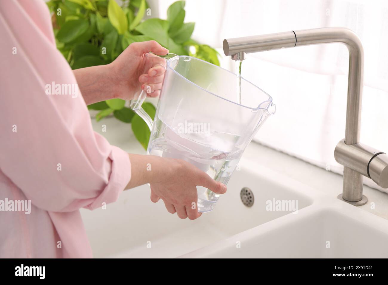 Donna che riempie la caraffa del filtro con acqua del rubinetto in cucina, primo piano Foto Stock