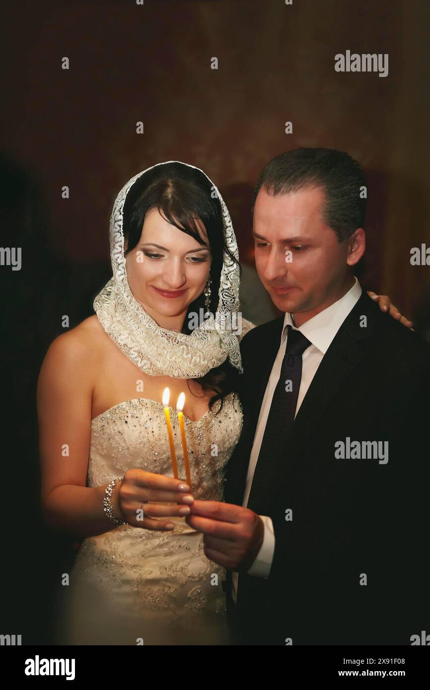 Uno sposo che tiene le candele accese durante una cerimonia nuziale, trasuda amore e felicità in un ambiente formale Foto Stock