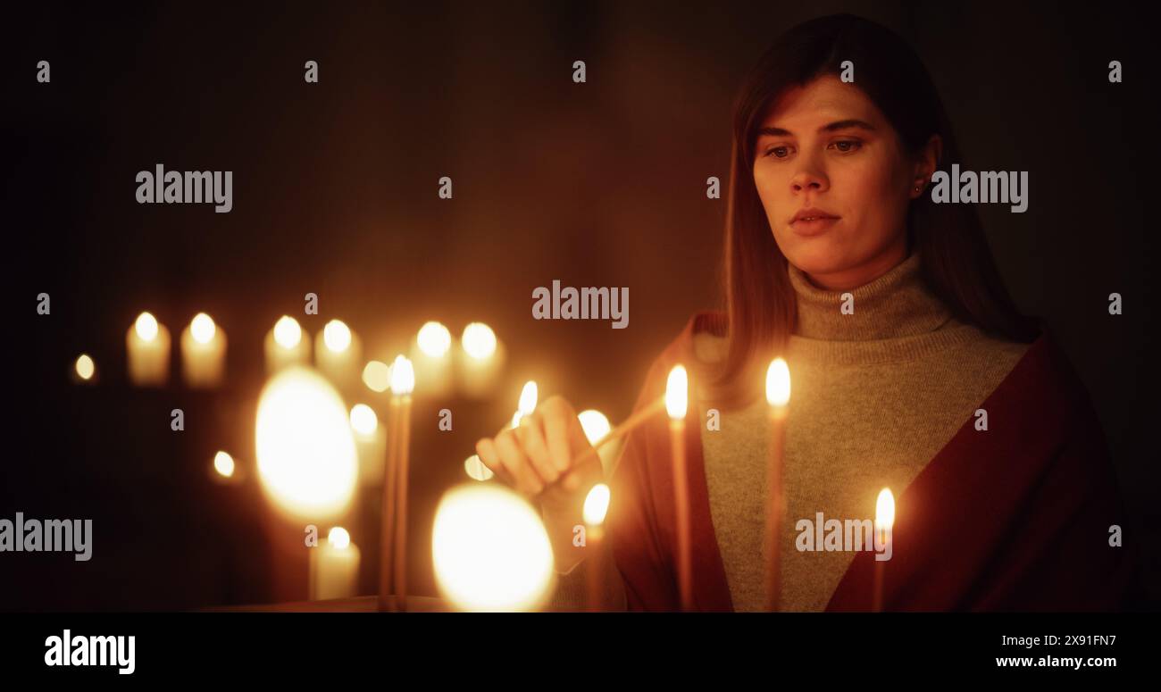 Devota donna cristiana che accende una candela nella Chiesa, pregando ed esprimendo devozione al Signore. Parrocchiana femminile che spera e si avvicina spiritualmente a Dio. Donna cristiana all'altare Foto Stock